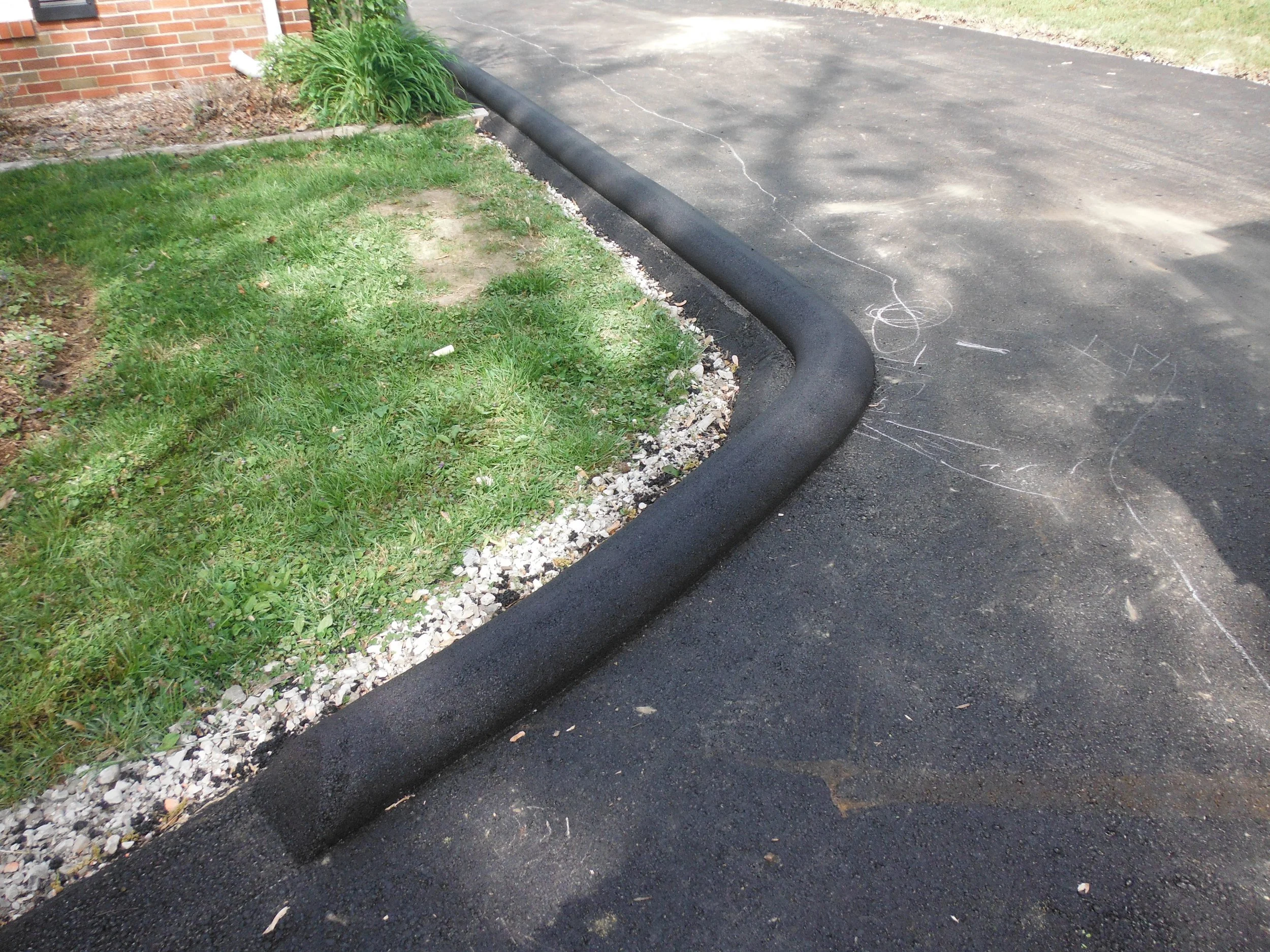 A black rubber curb stops the edge of a manicured lawn next to a paved driveway.