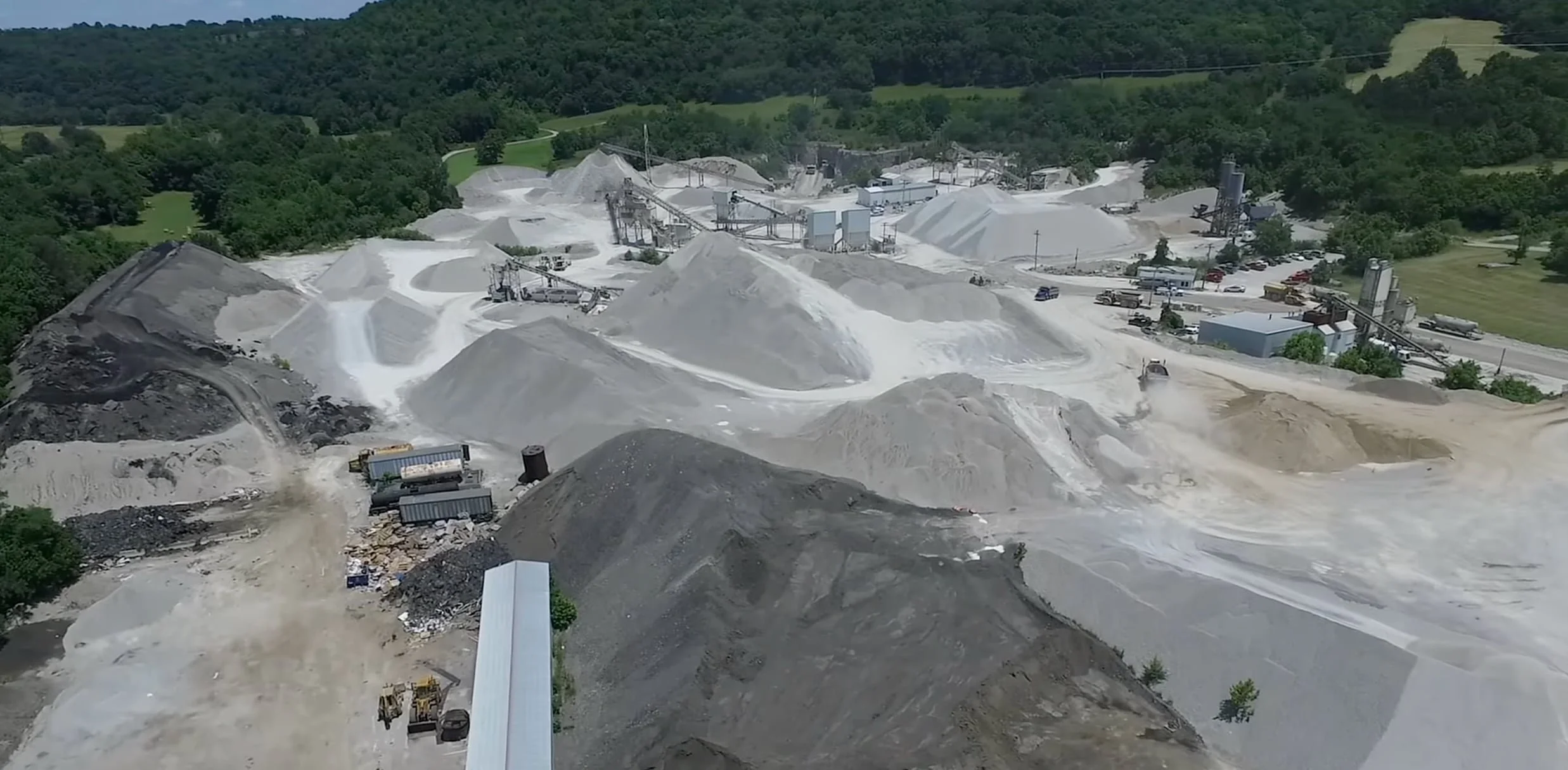 asphalt plant with mountains of rock of different sizes and colors. refiners and trucks show throughout the image