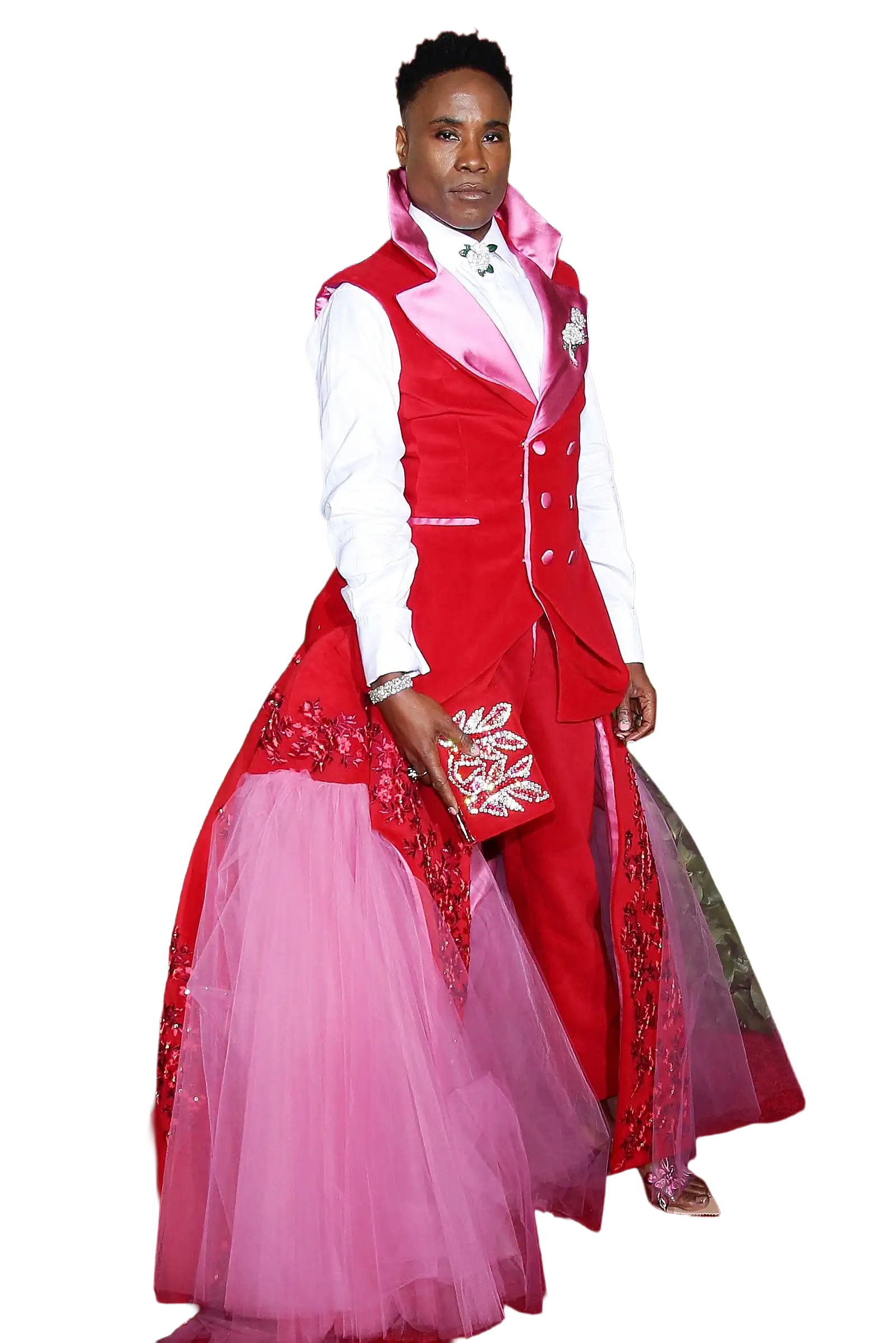 Person wearing a red and pink layered gown with floral embroidery, holding a matching clutch, standing against a black background. The Valentine's Museum NYC Valentine's Day Event.