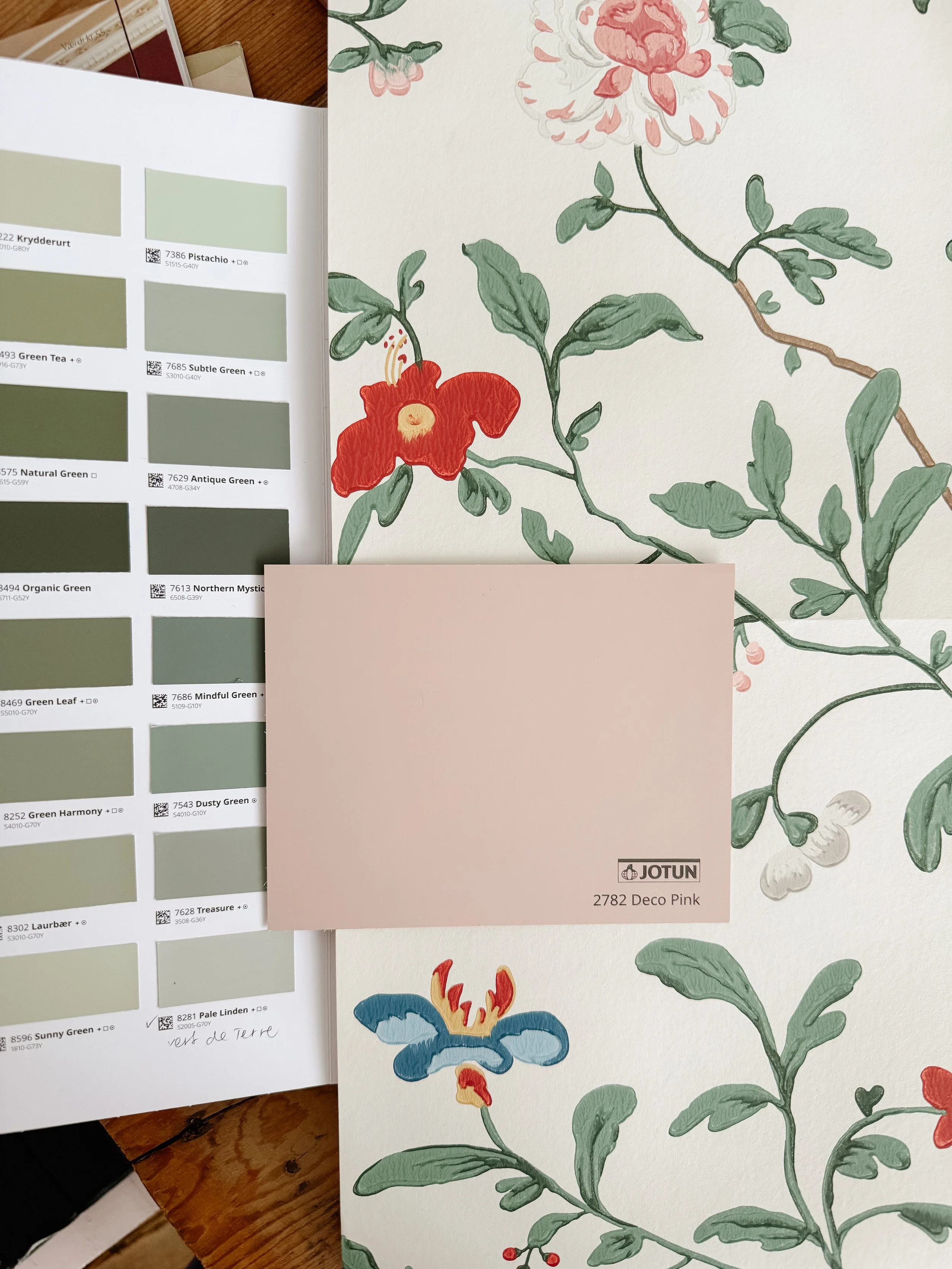 A botanical illustration of various flowers and leaves on a cream-colored background. A prominent red flower with yellow anthers, a pink peony, and a blue flower with red and yellow details are visible. Color swatches for different shades of green an