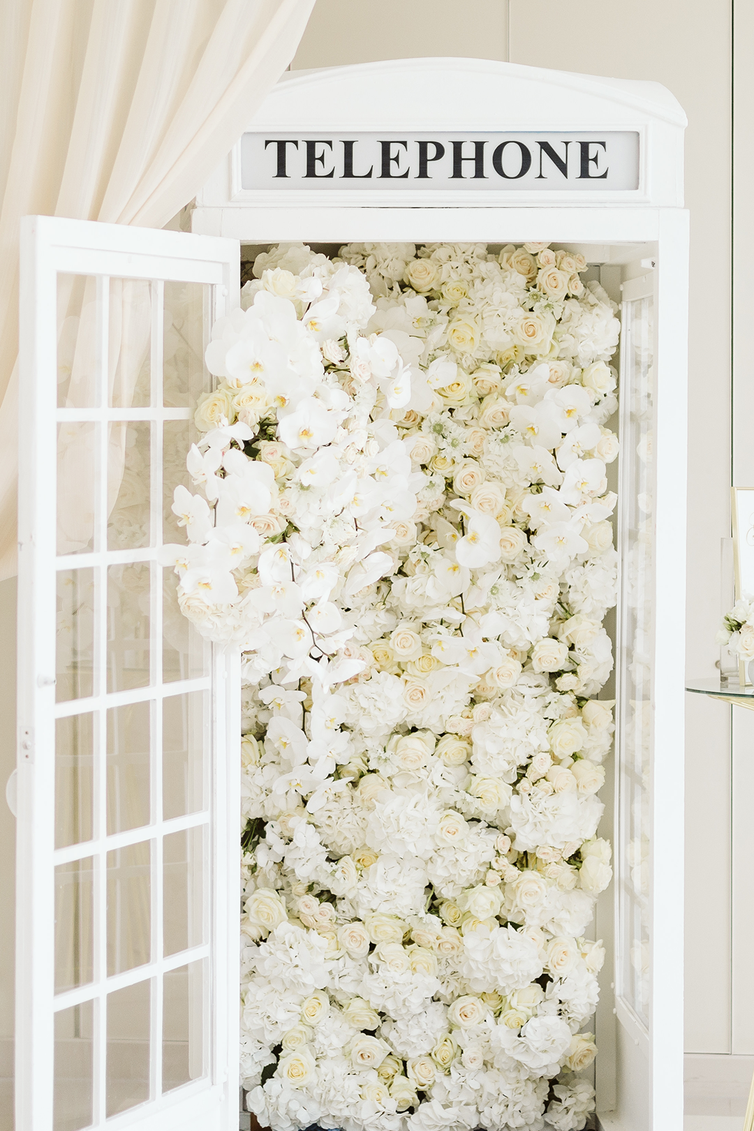 Wedding Photo Booth of a British telephone box painted white and filled with white roses and orchids, Cliveden House, UK.
