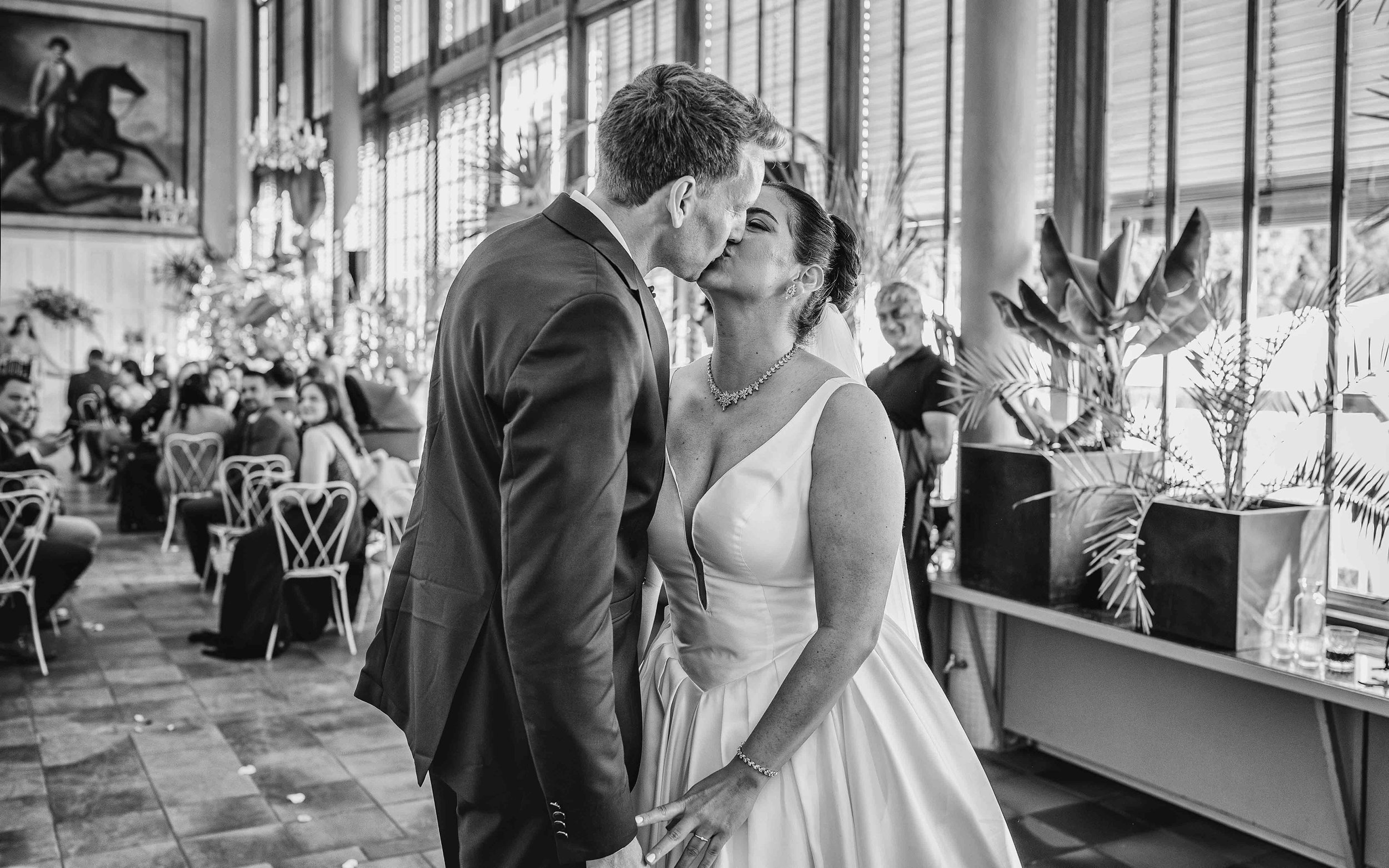 Ein Brautpaar küsst sich bei einer Hochzeit in einem festlichen Hallenraum.