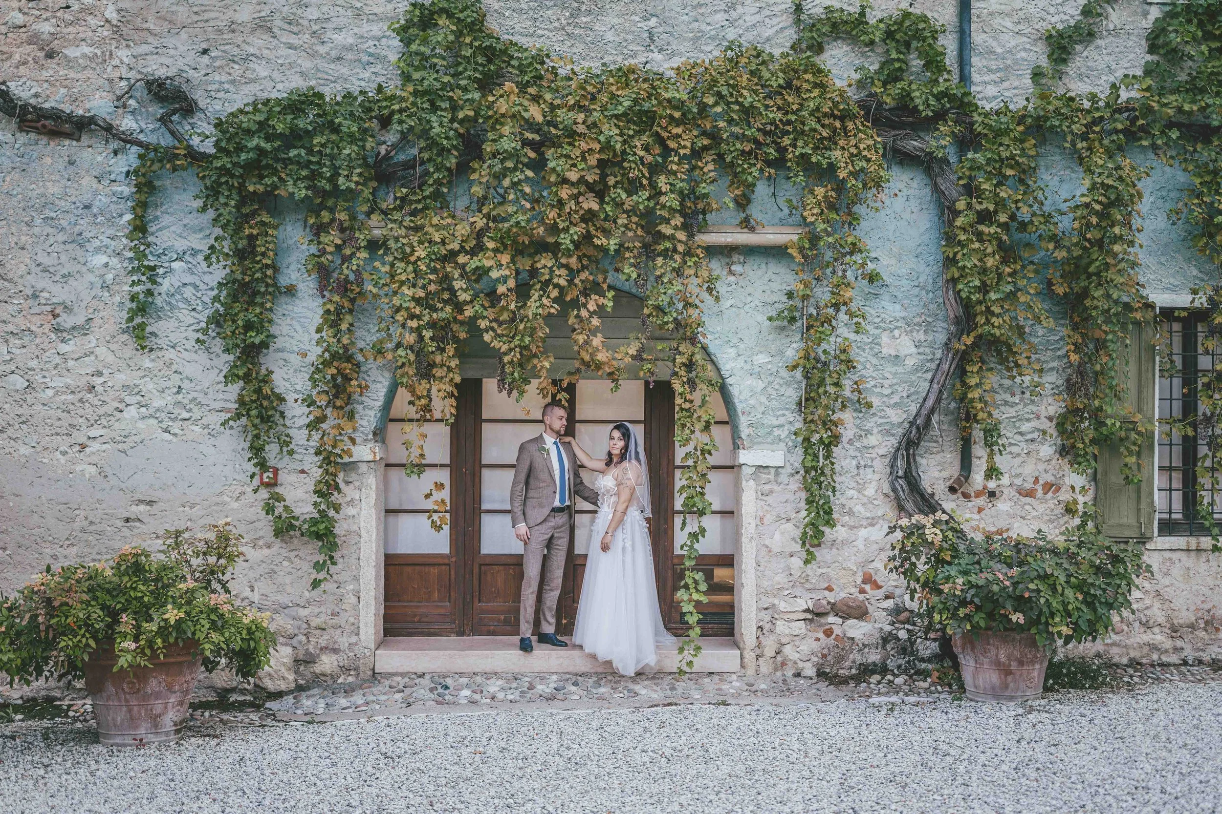 Ein Brautpaar steht im Park, mit den Stirn aneinander, die Braut hält einen Blumenstrauß, beide lächeln sanft.