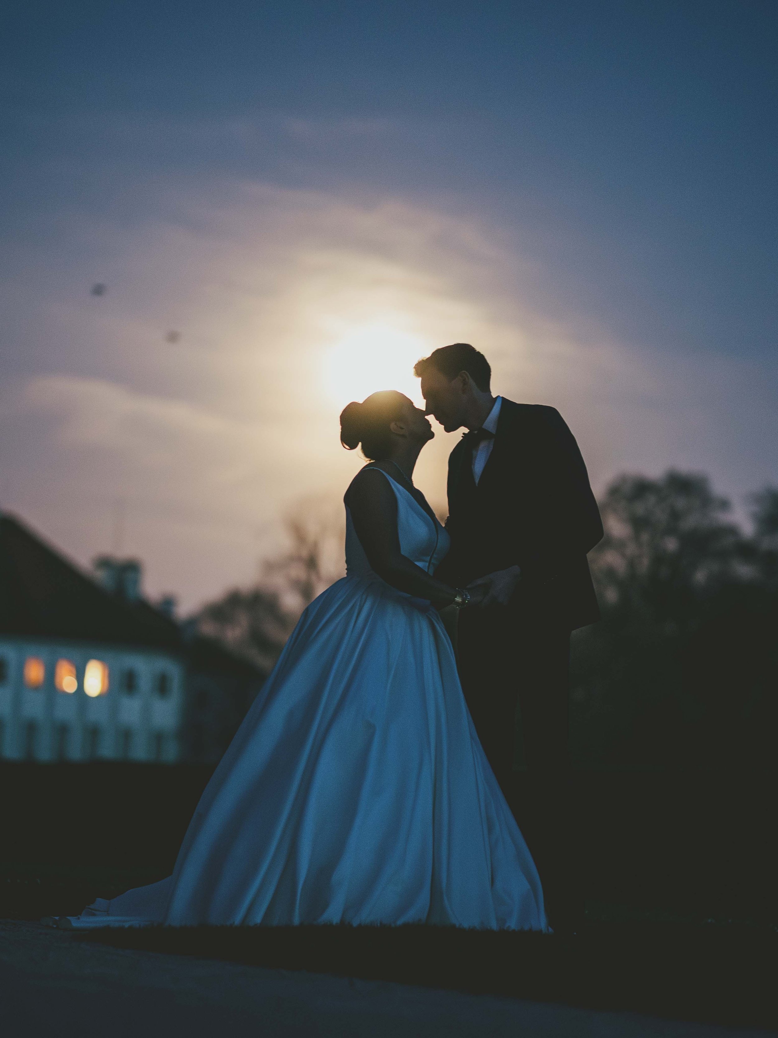 Ein Hochzeitsfoto eines Paares, das sich bei Sonnenuntergang küsst, mit einem dunklen Himmel im Hintergrund.