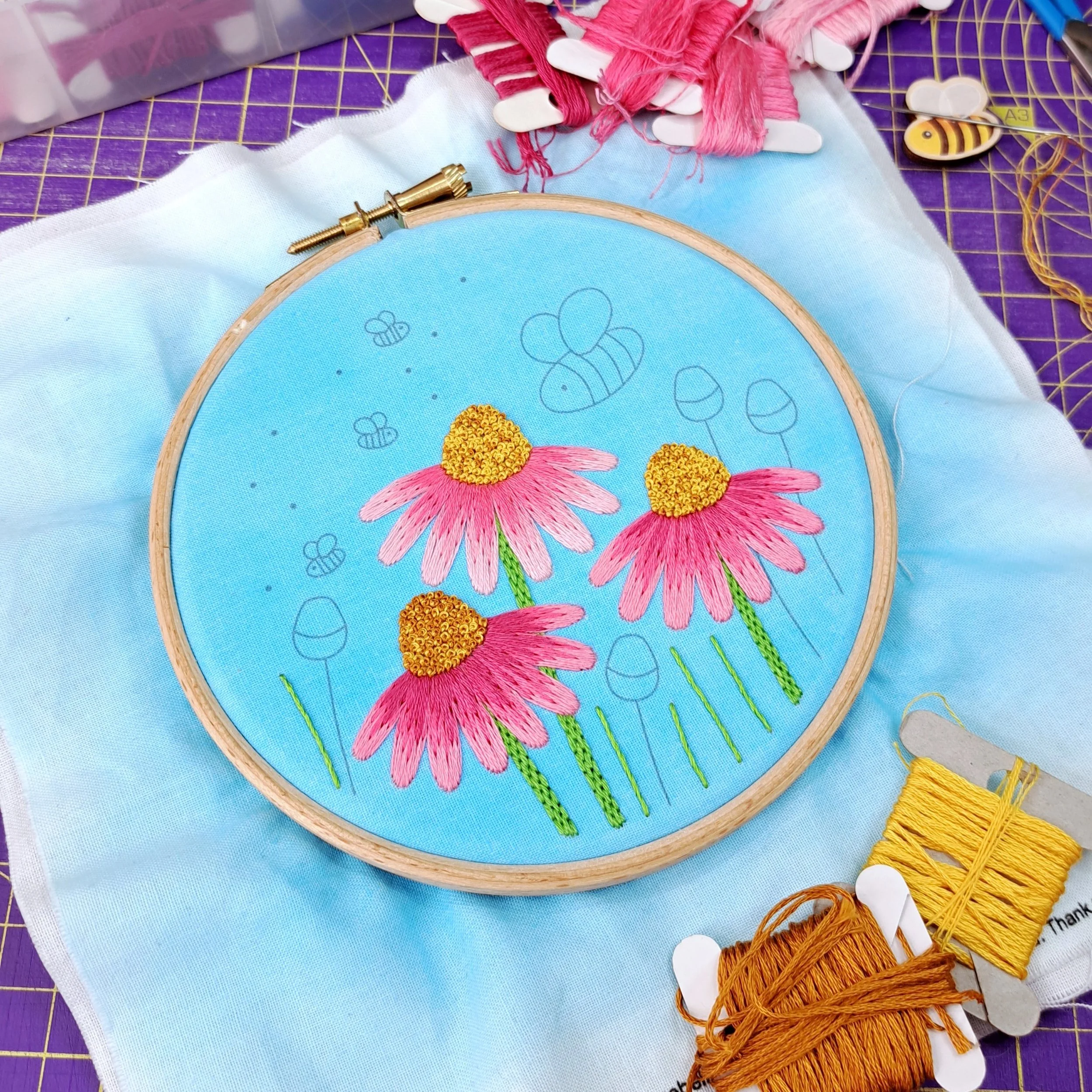 Partly completed embroidery of the flower and bee design. All three of the Echinacea flowers and the grass blades have been stitched.