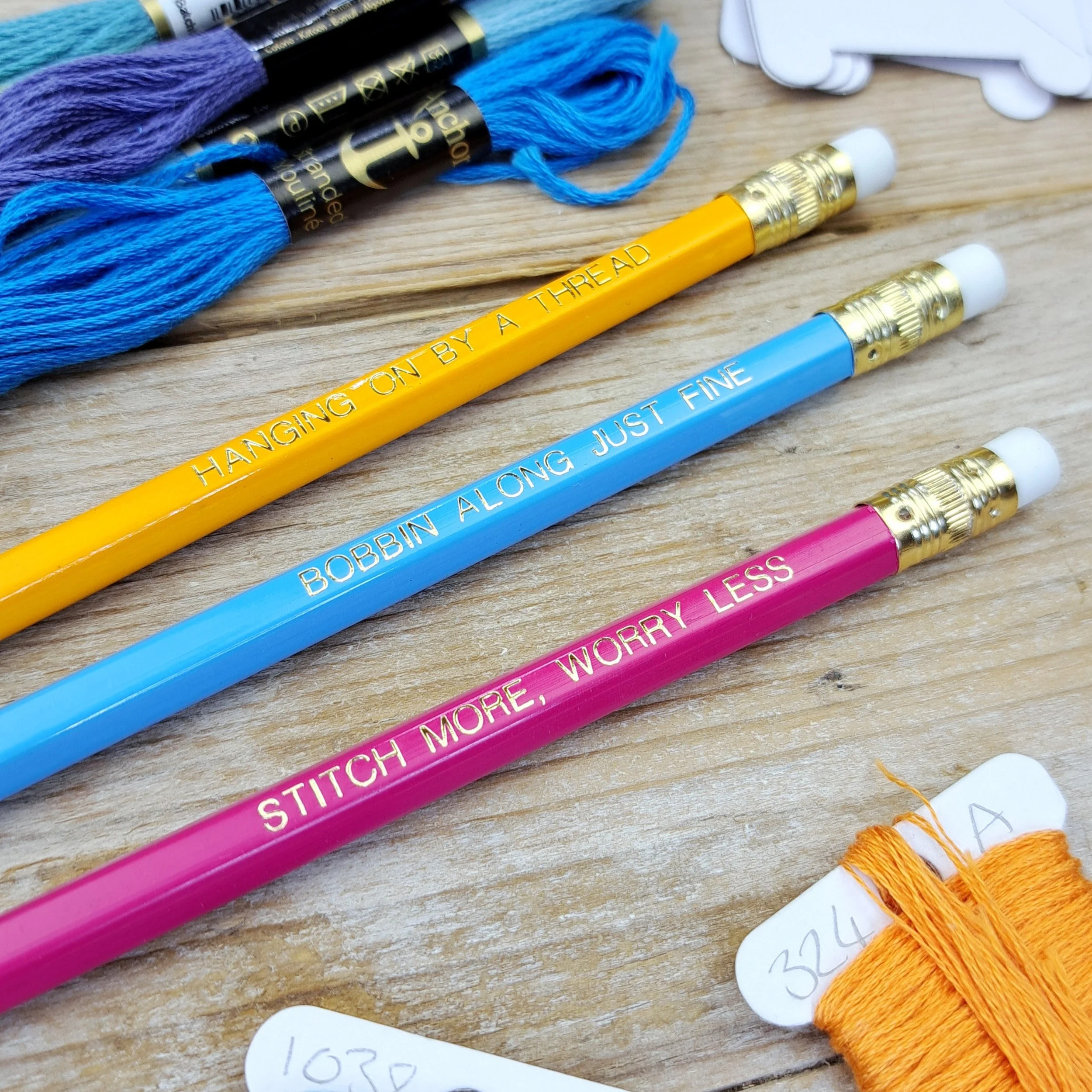 Three stitchy pencils showing the gold foil slogans and erasers from a side angle