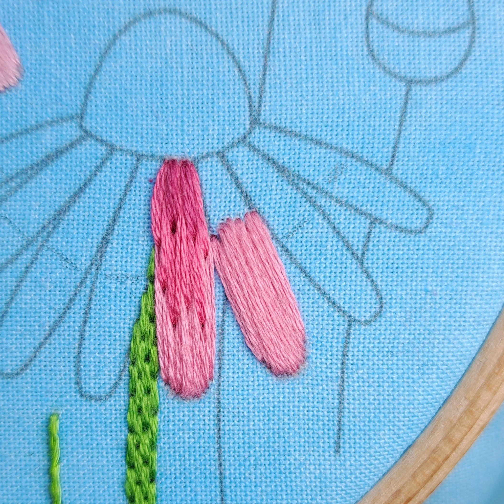 Close-up of light pink satin stitch embroidered on the outer sections of the right-hand echinacea flower petals.