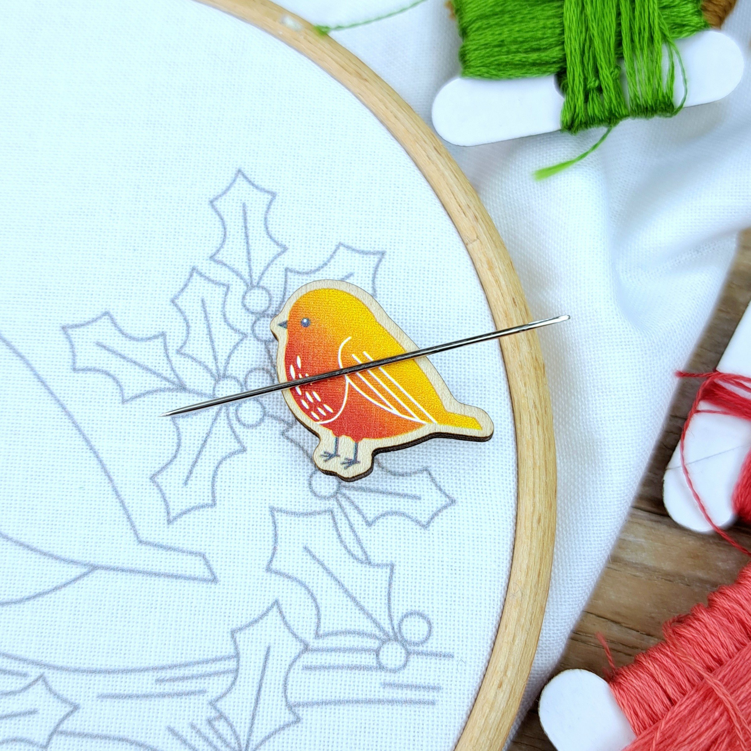 Close-up of a small red and yellow robin wooden magnetic needle minder holding an embroidery needle.