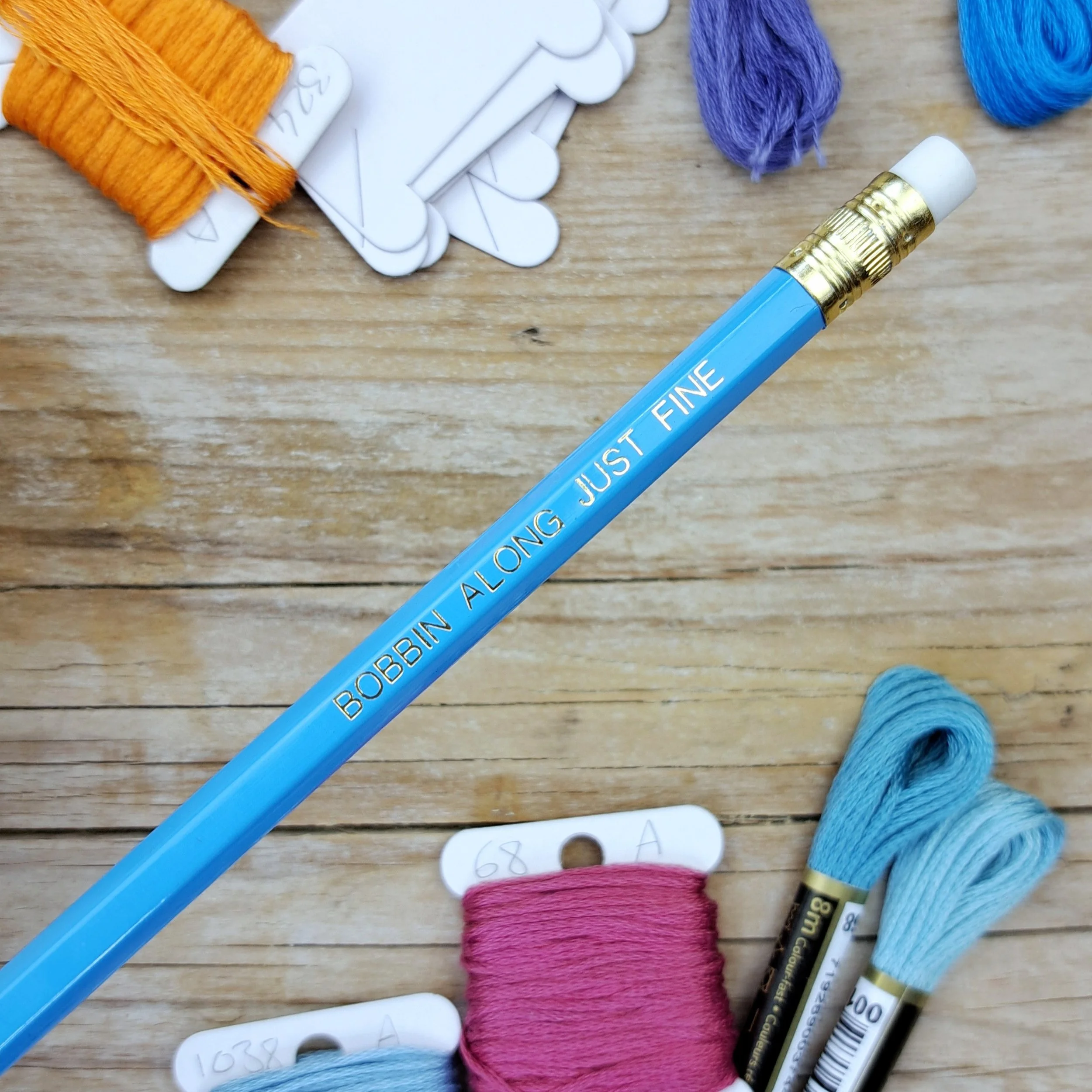 Blue "Bobbin Along Just Fine" HB pencil showing the gold foil slogan, gold ferrule and white eraser