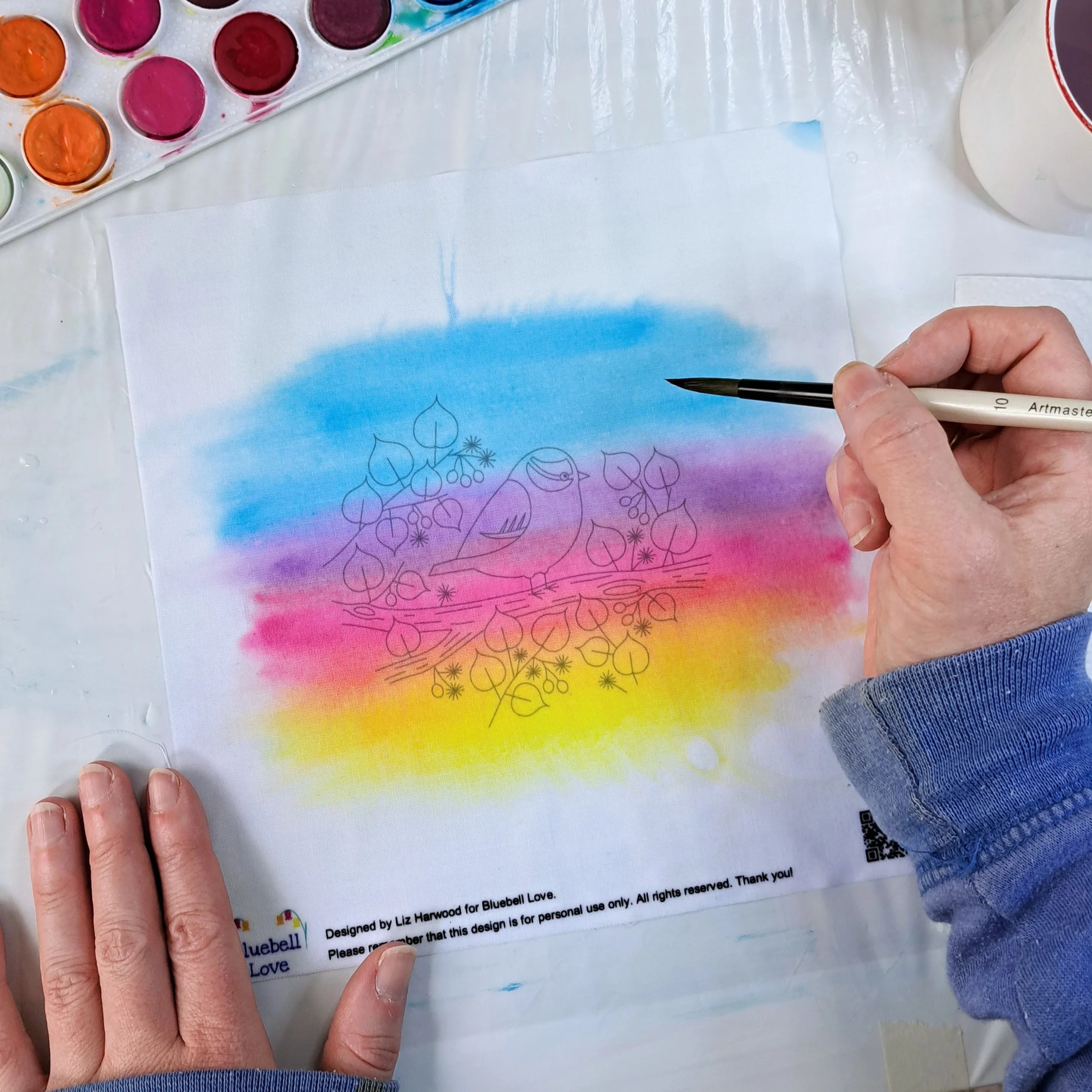 My hand painting the next colour band of sunrise to the fabric embroidery panel. There is now a band of yellow at the bottom, blending upwards into orange, then into pink, then purple, and finally into blue at the top.