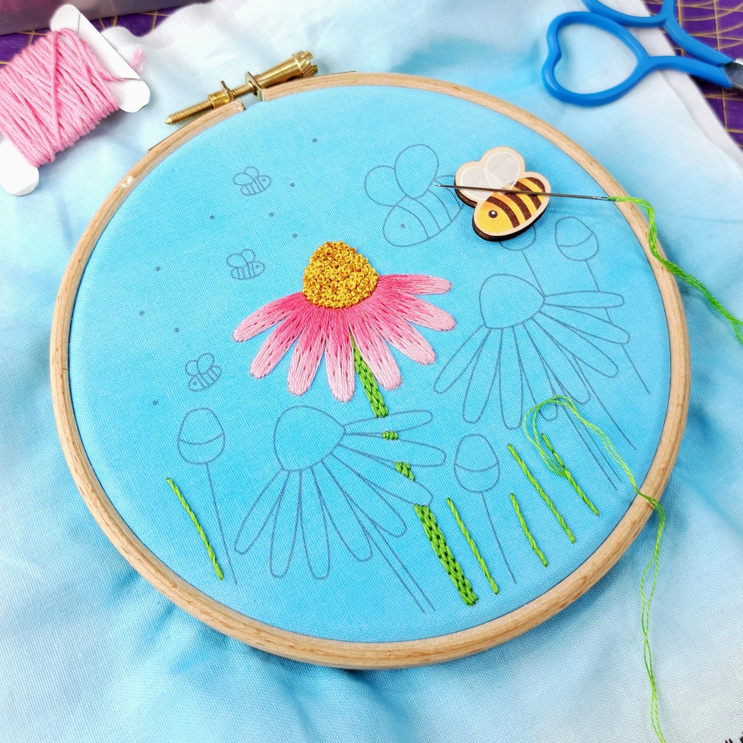Partly completed embroidery of the flower and bee design. The middle Echinacea flower and the grass blades have been stitched.