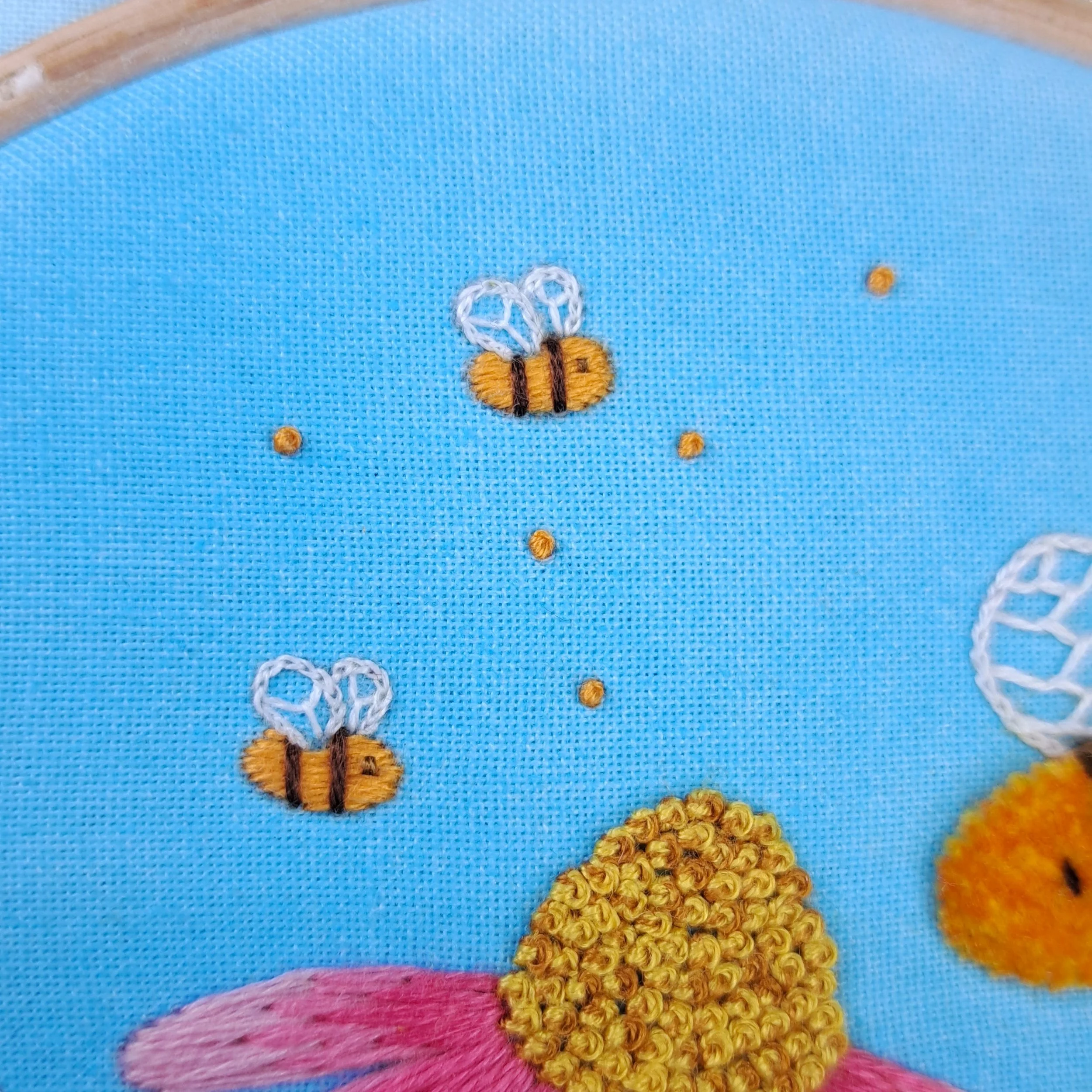 Close-up of the orange French Knots used to embroider the flying distant bees.