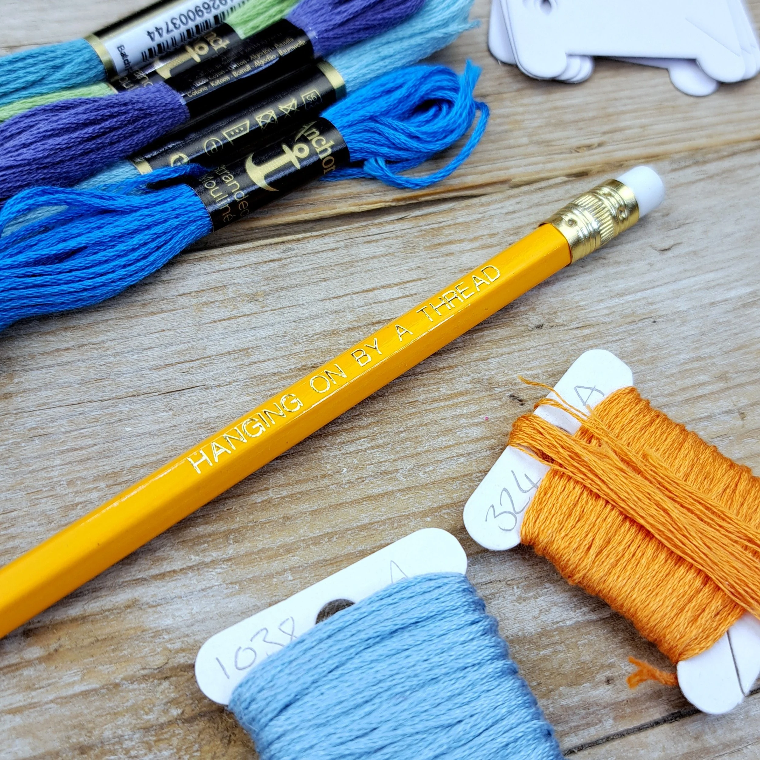 Angled close-up of the orange "Hanging on by a Thread" HB pencil with gold foil slogan