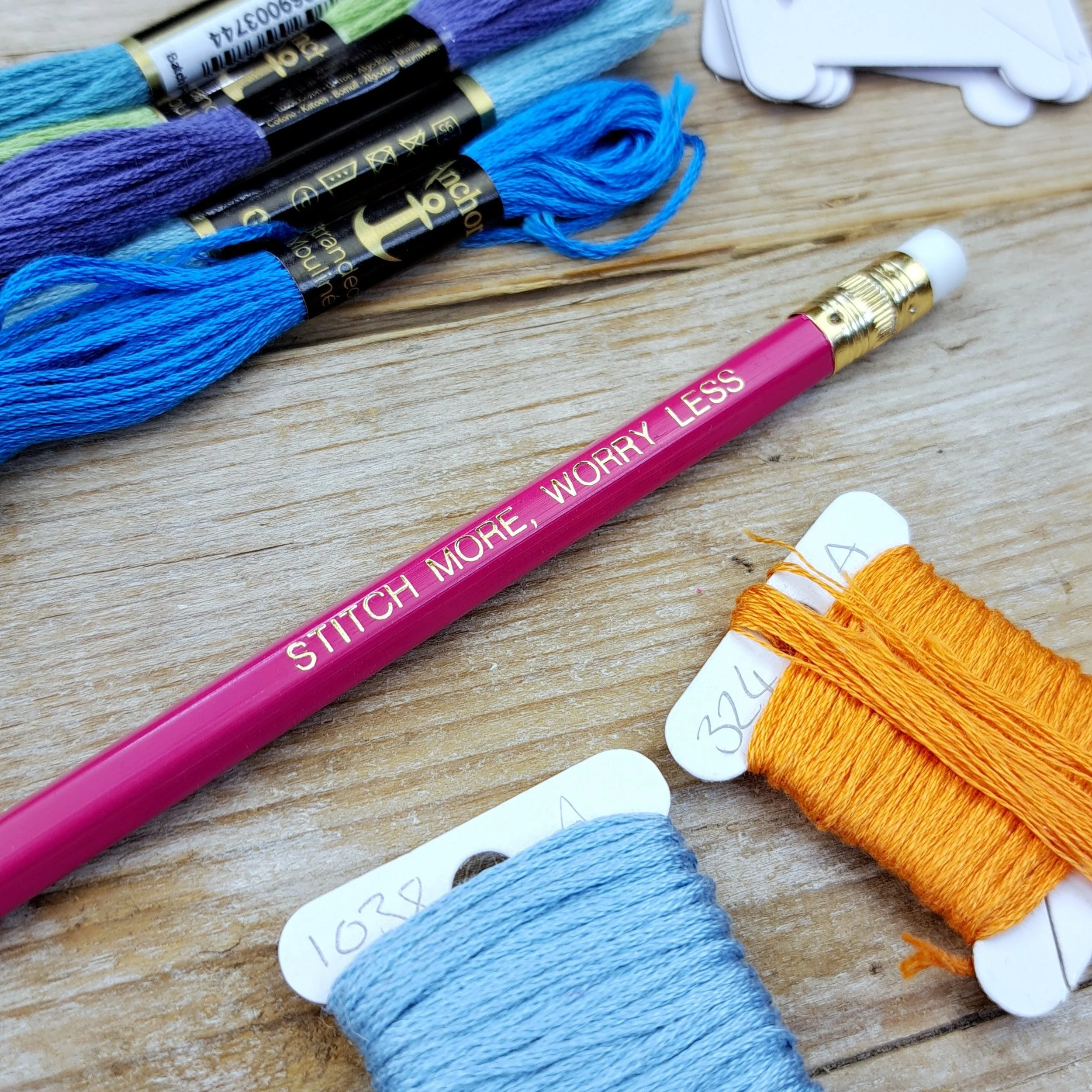 Angled close-up of the pink "Stitch More, Worry Less" HB pencil with gold foil slogan