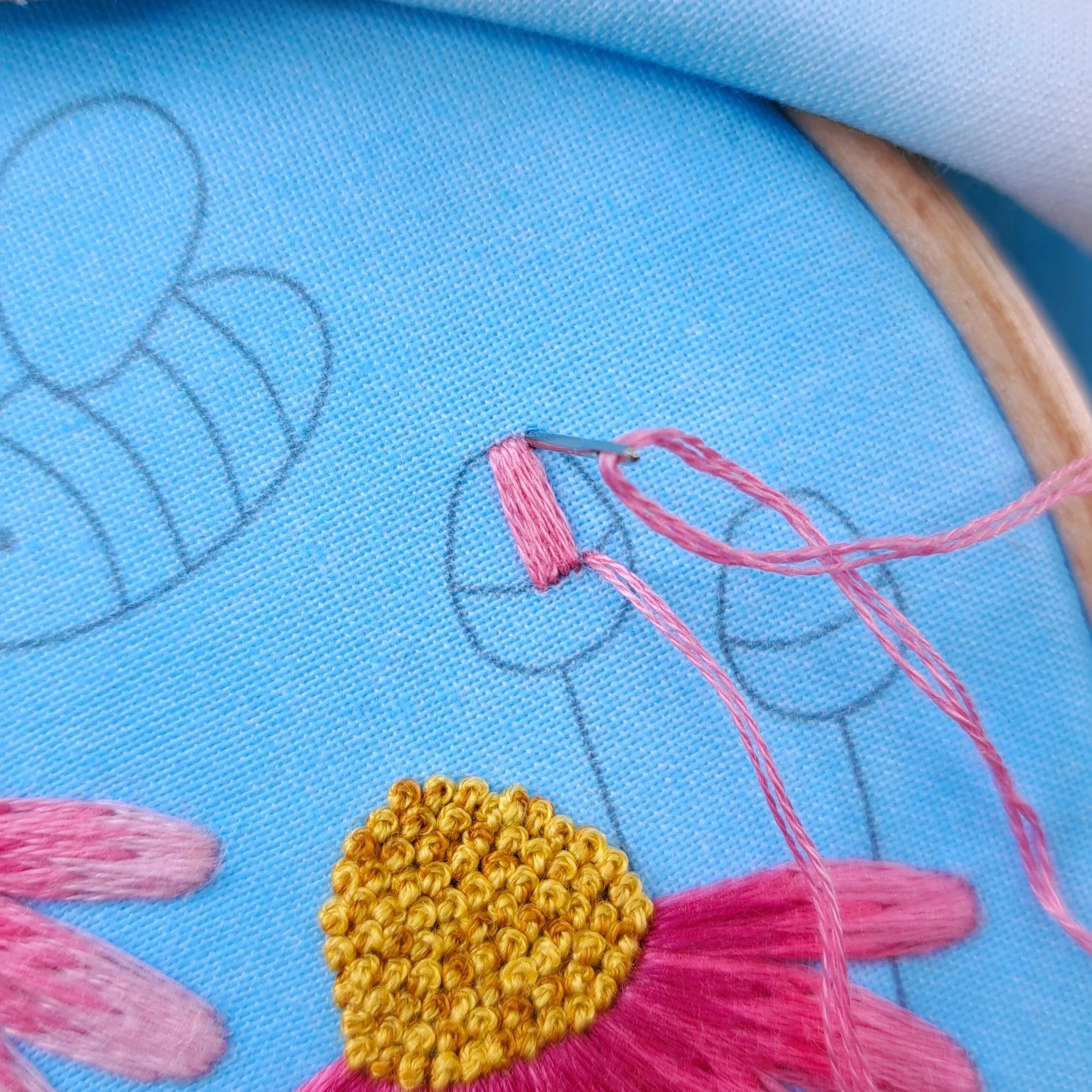 Close-up of pink Satin Stitch being embroidered on the top part of a flower bud.
