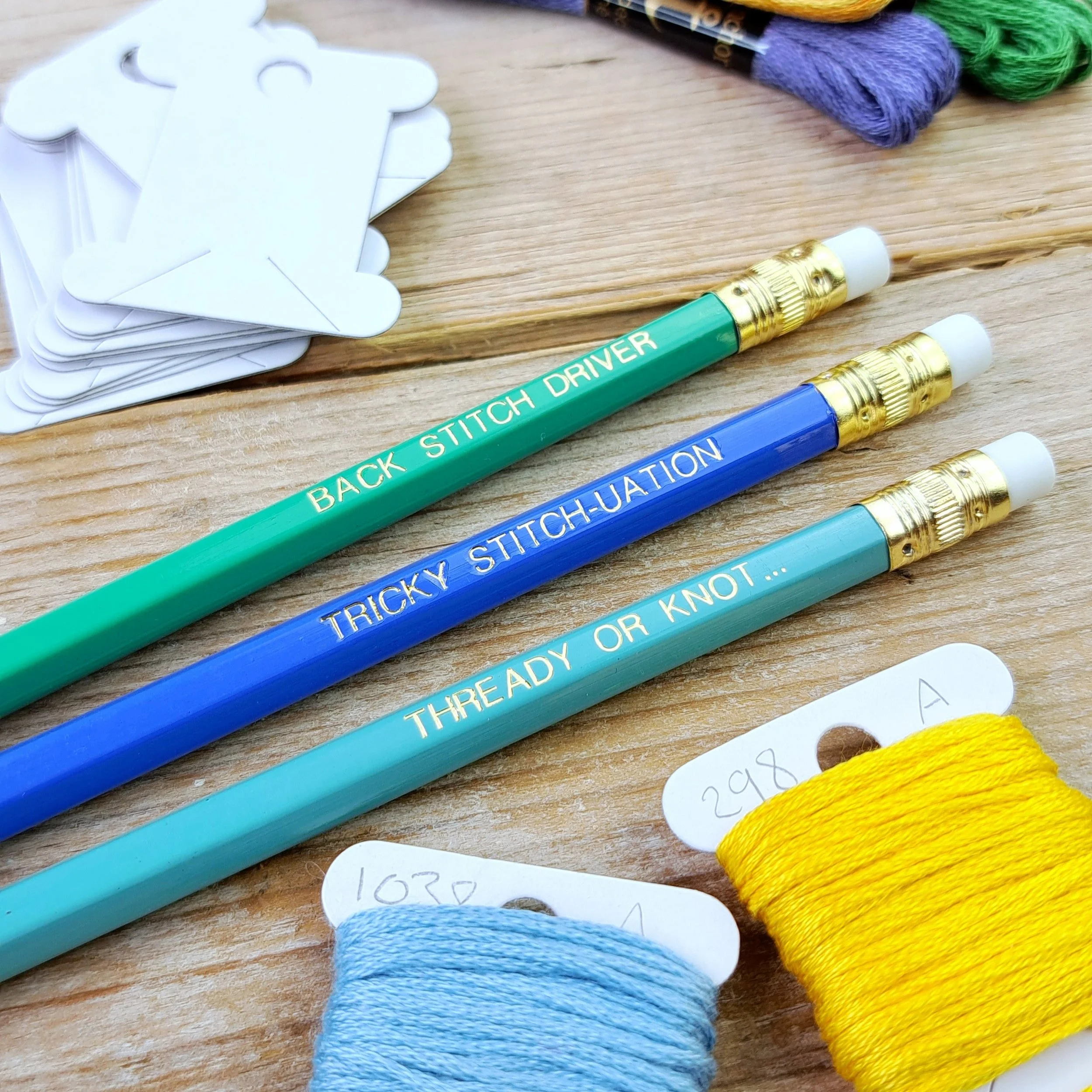 Three stitchy pencils showing the gold foil slogans and erasers from a side angle