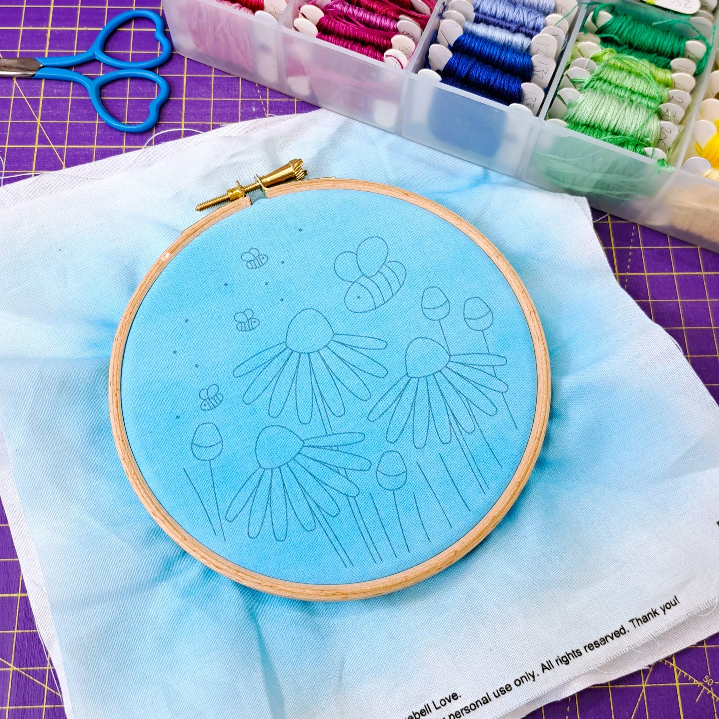 The painted flower and bee embroidery panel dried and placed neatly in a 5-inch wooden embroidery hoop, ready to begin stitching.