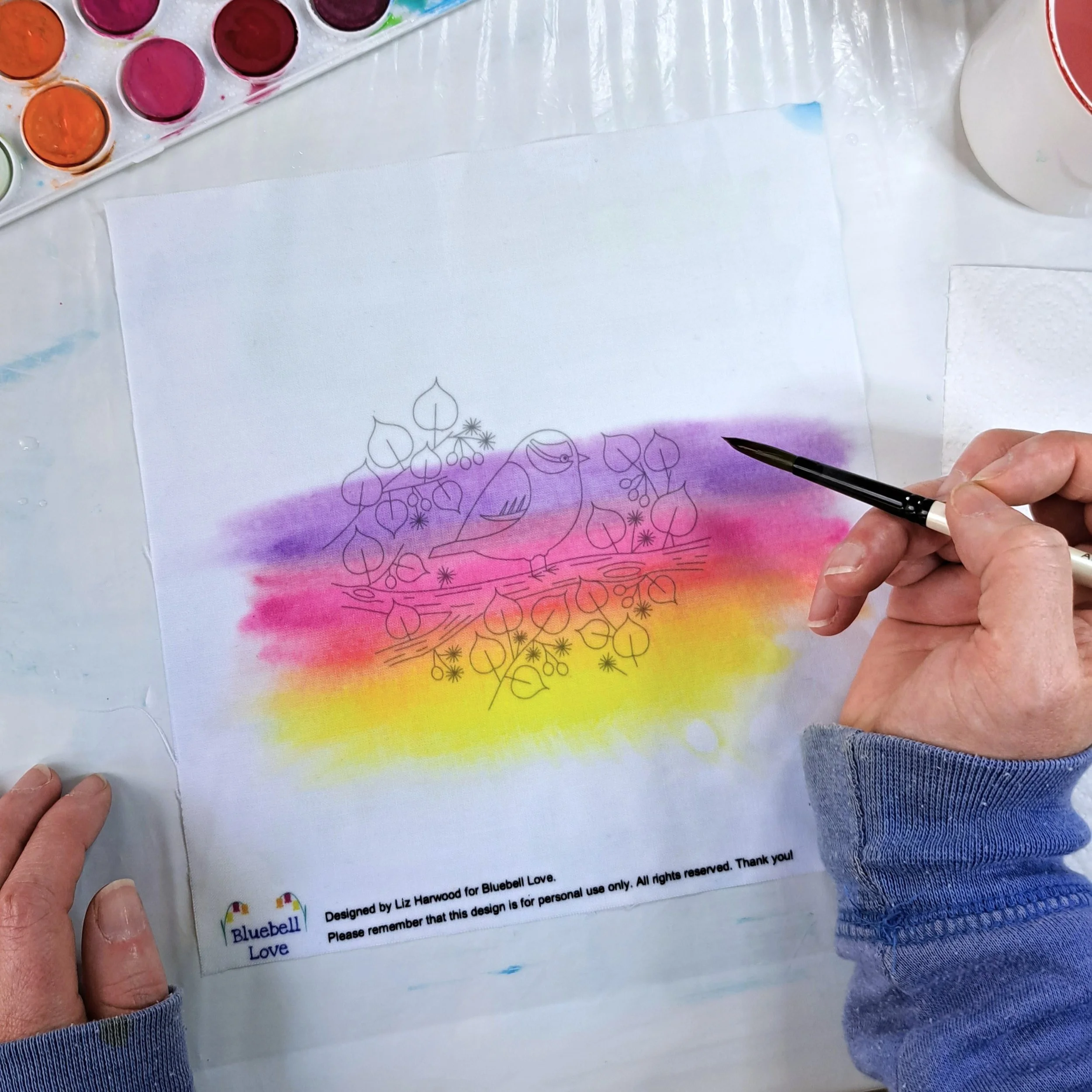 My hand painting the next colour band of sunrise to the fabric embroidery panel. There is now a band of yellow at the bottom, blending upwards into orange, then into pink, and then purple.