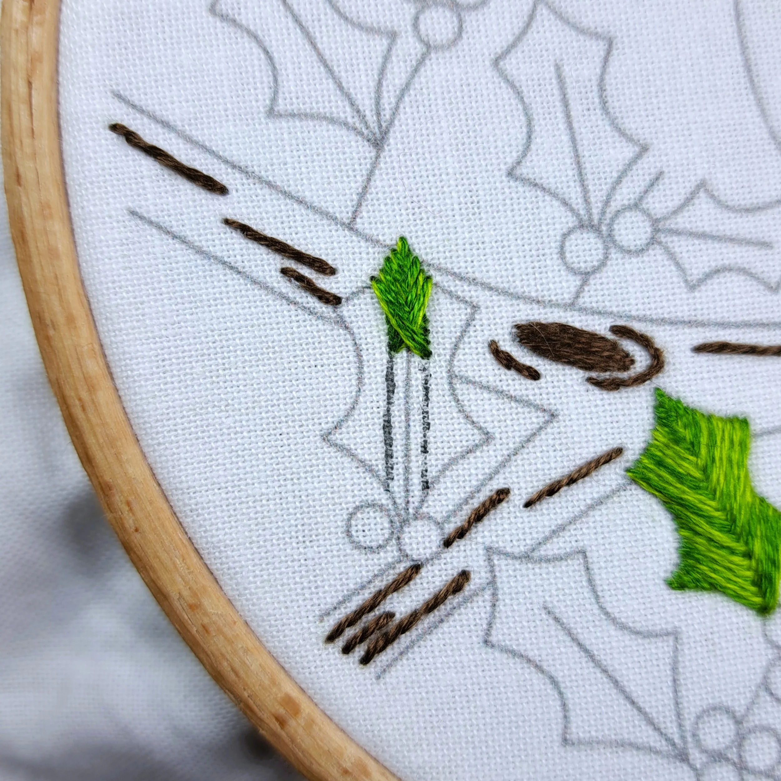 Close-up of a holly leaf with green Fishbone Stitches stitched about halfway down.