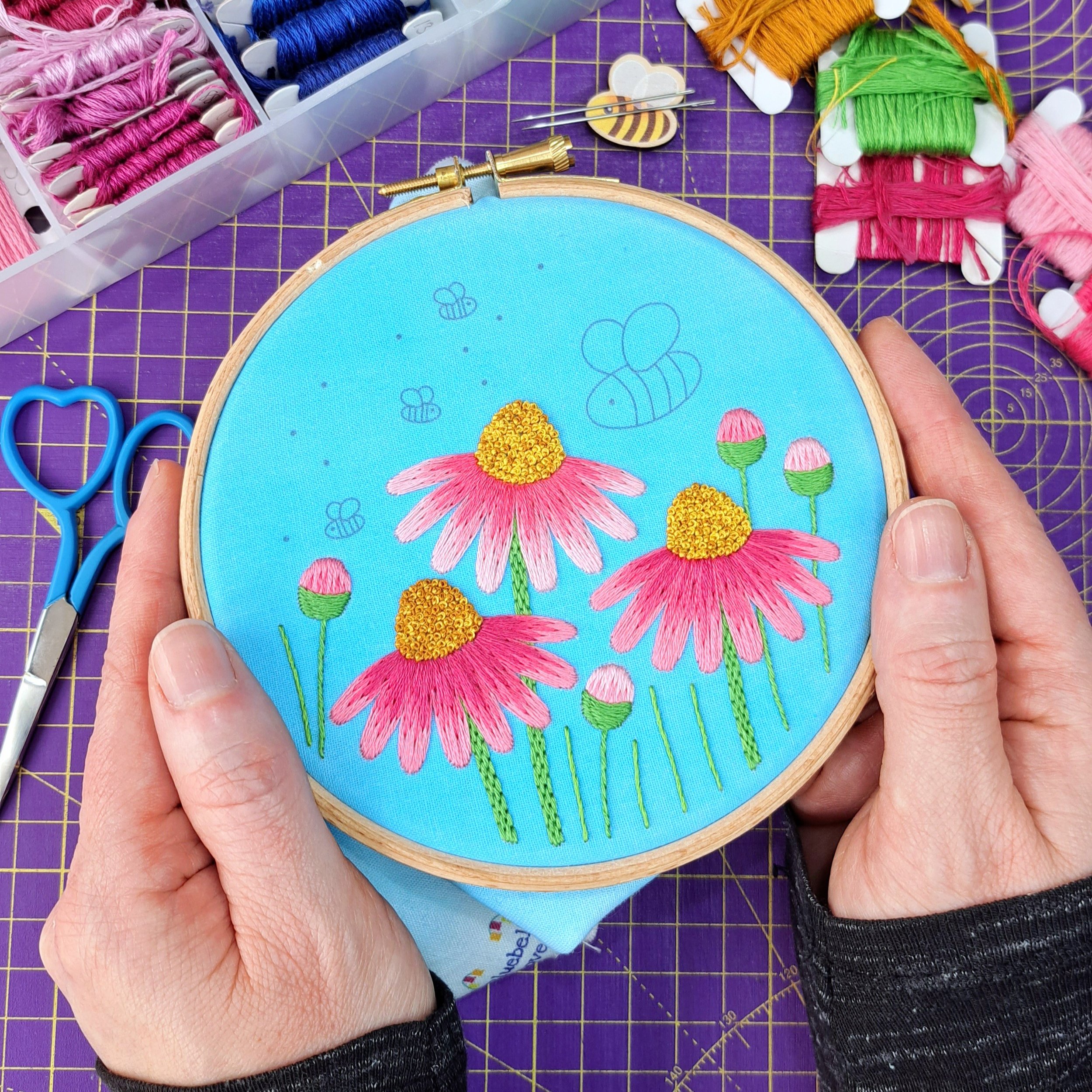 Partly completed embroidery of the flower and bee design. All three of the Echinacea flowers, the grass blades, and the flower buds have been stitched.