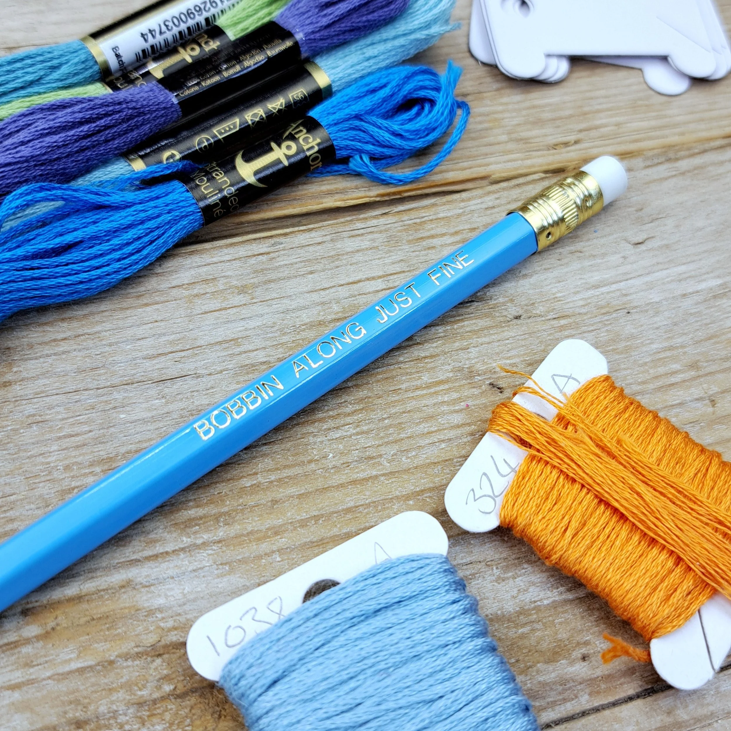 Angled close-up of the blue "Bobbin Along Just Fine" HB pencil with gold foil slogan.