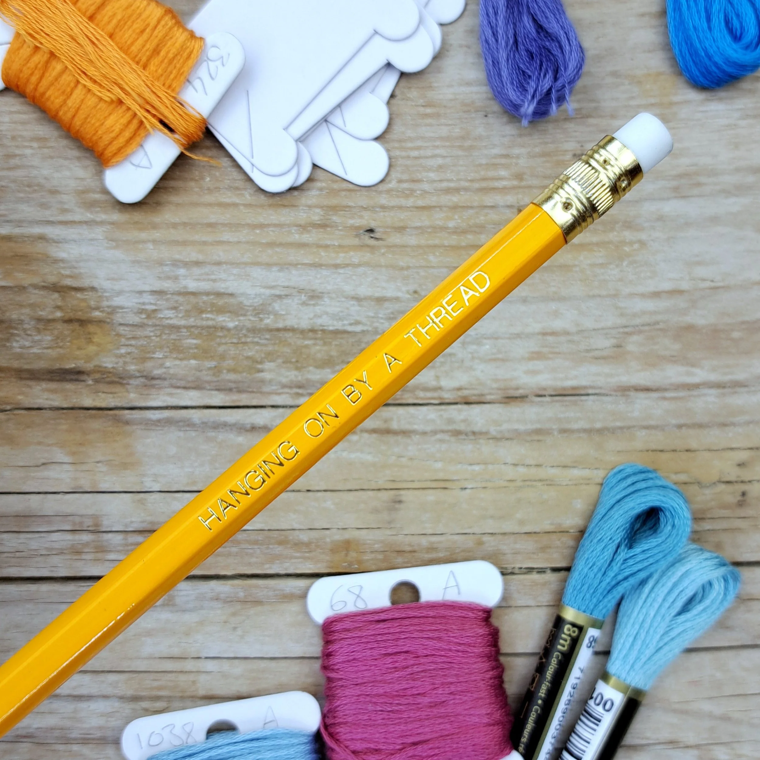 Orange "Hanging on by a Thread" HB pencil showing the gold foil slogan, gold ferrule and white eraser