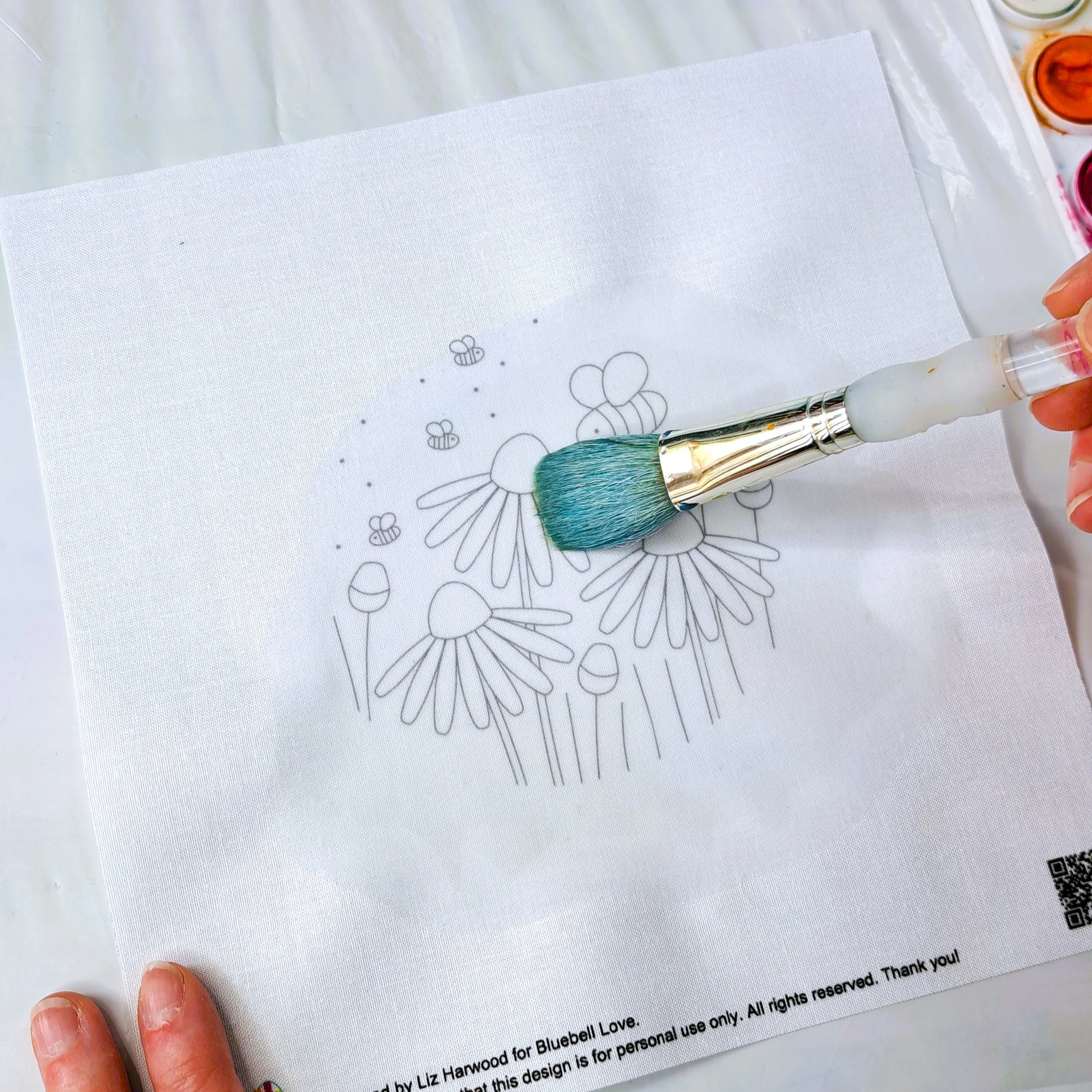 A large round paint brush being used to paint clean water onto the fabric panel.