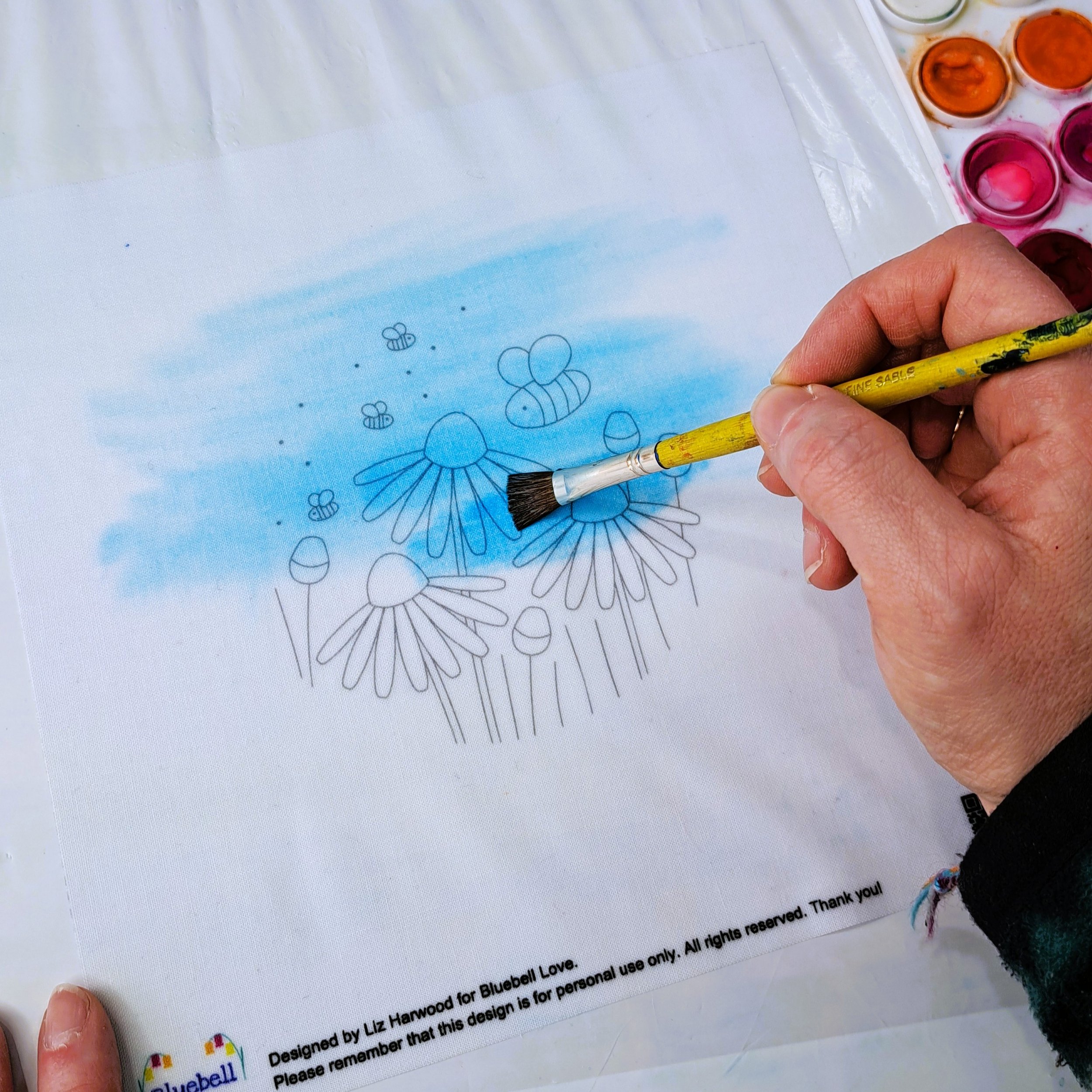 A paint brush being used to paint bright blue watercolour paint on to the fabric embroidery panel.