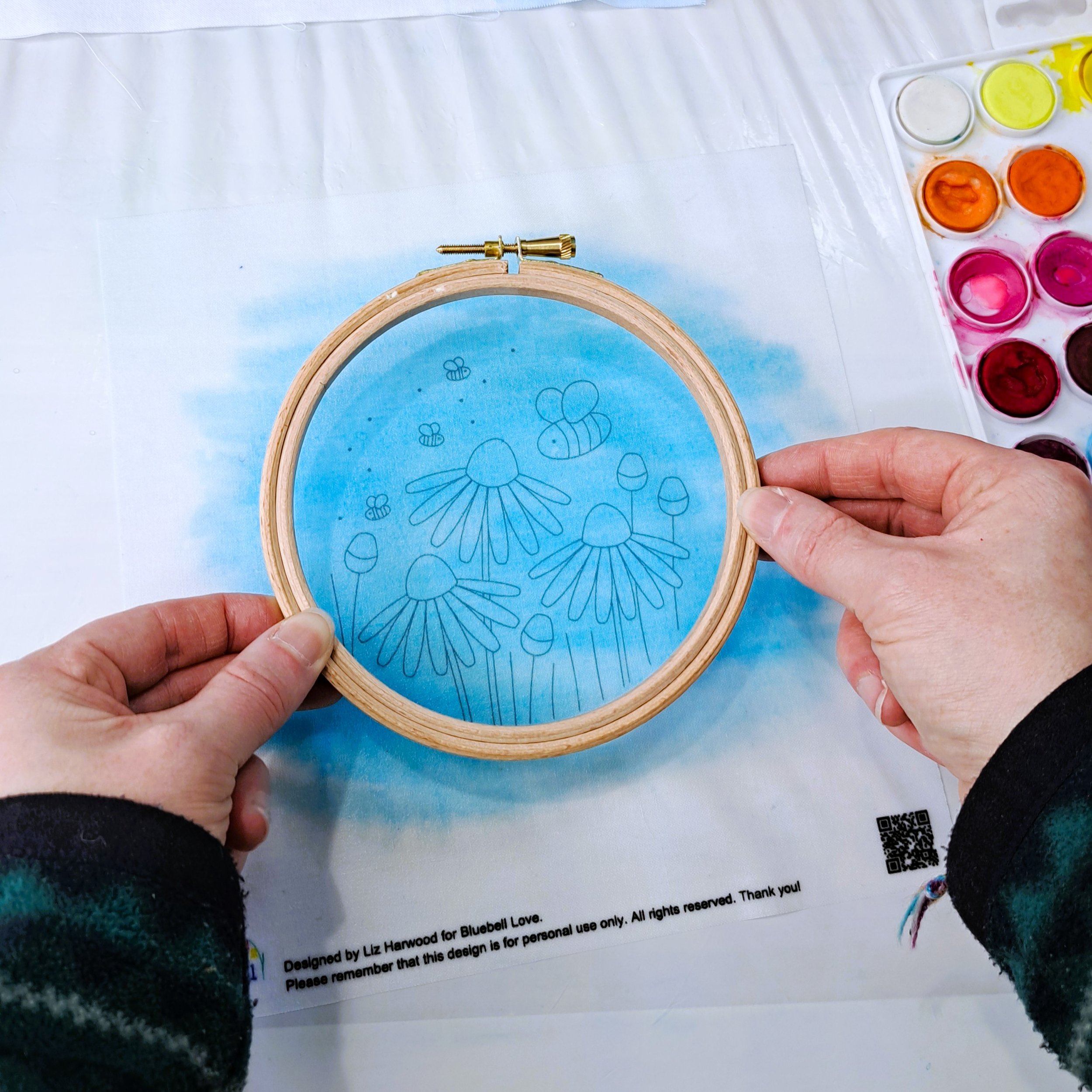 An embroidery hoop being held over the painted fabric panel to make sure it has been fully painted.