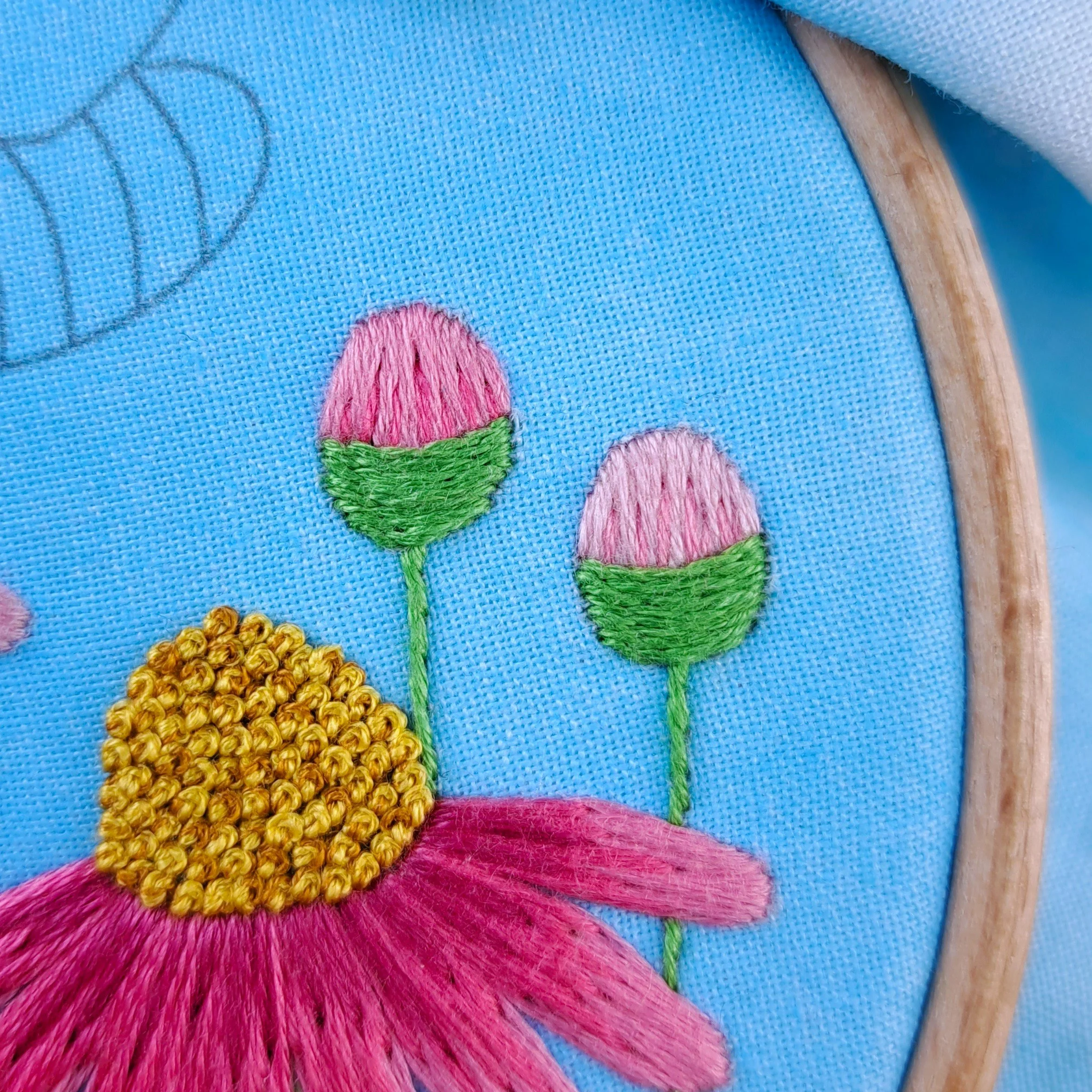 Close-up of two embroidered flower buds. One is stitched using darker pinks, and the other stitched using lighter pinks.