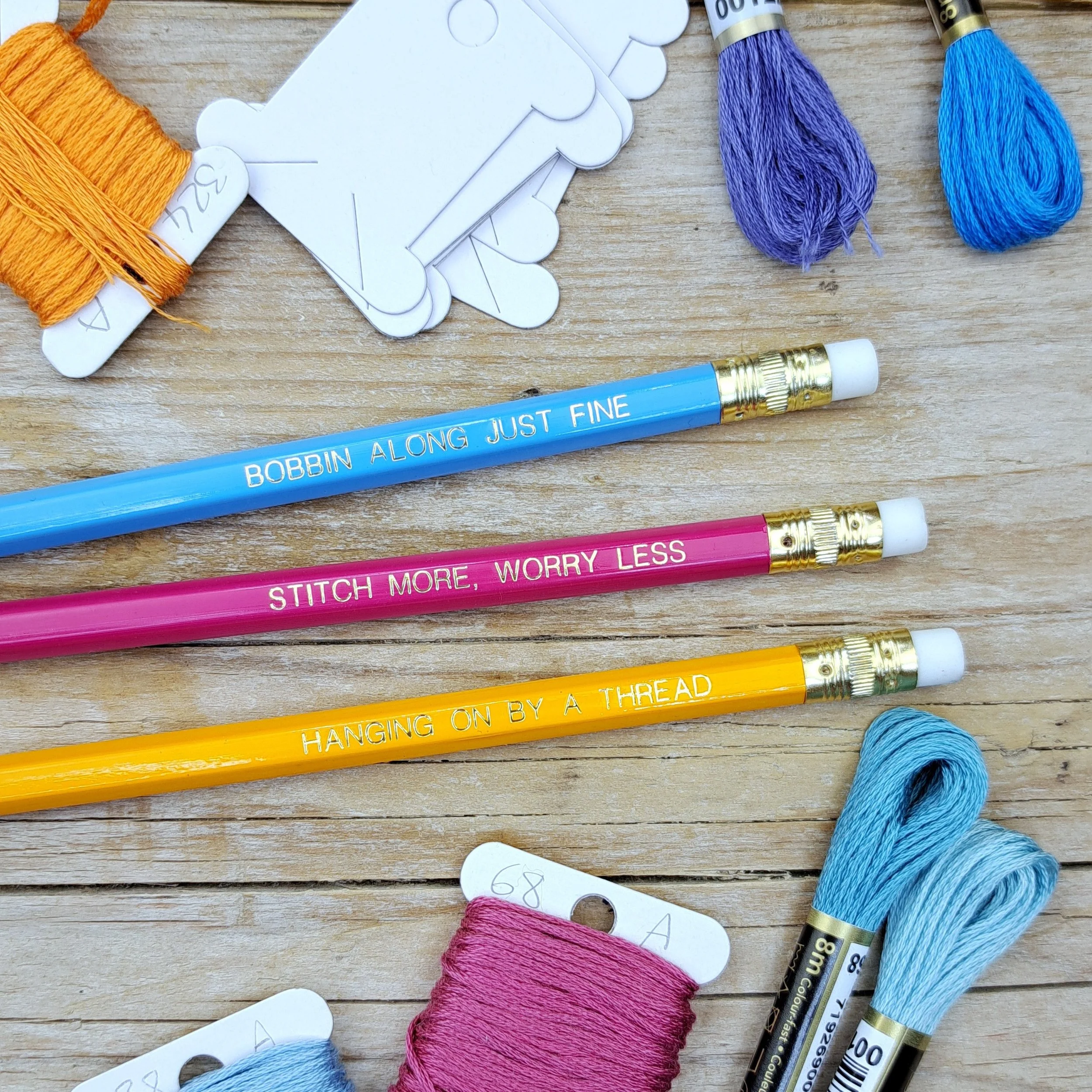 Three stitchy pencils showing the gold foil slogans and erasers in a flat lay