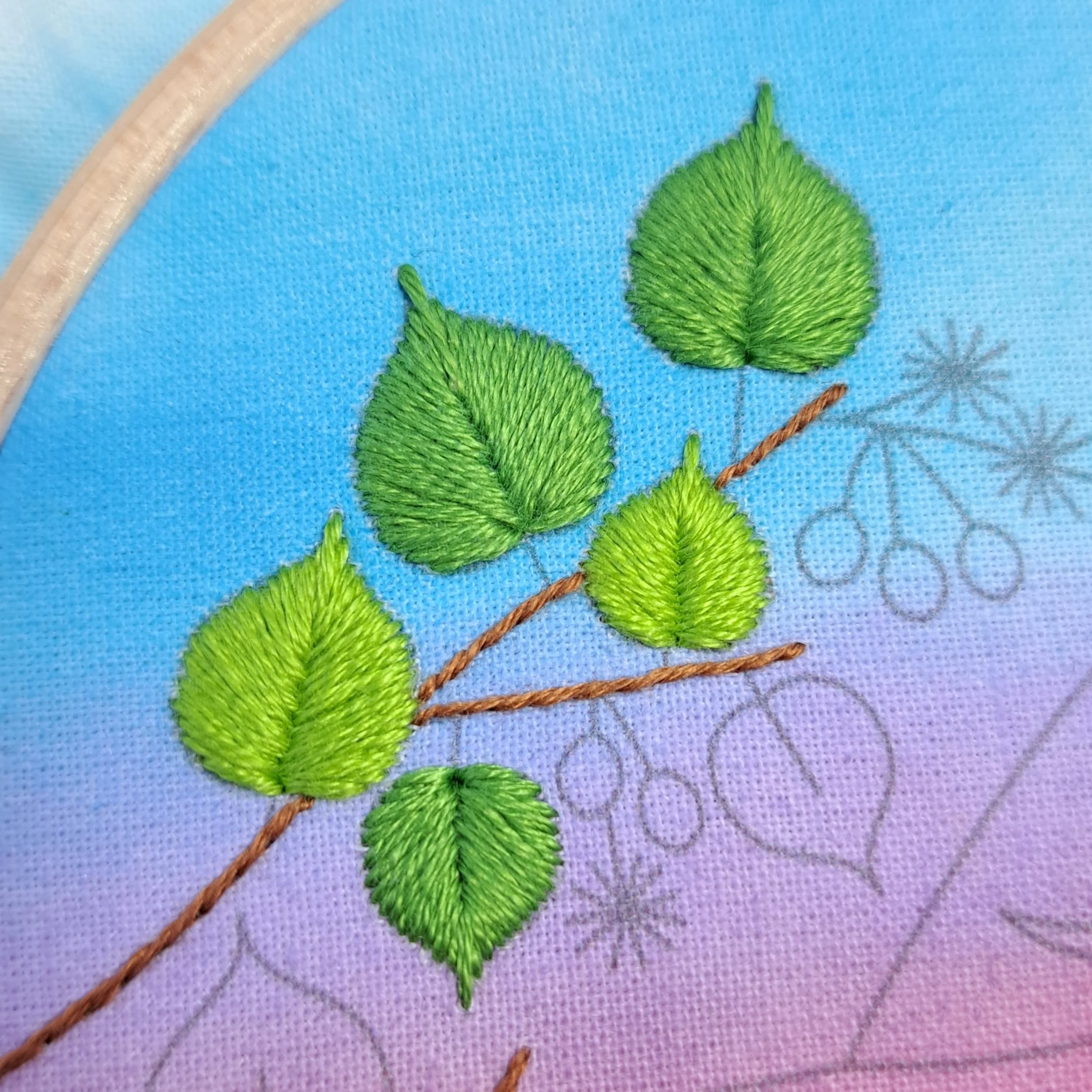 Close-up of five leaves on the tree branch embroidered with Leaf Stitch using three shades of green.