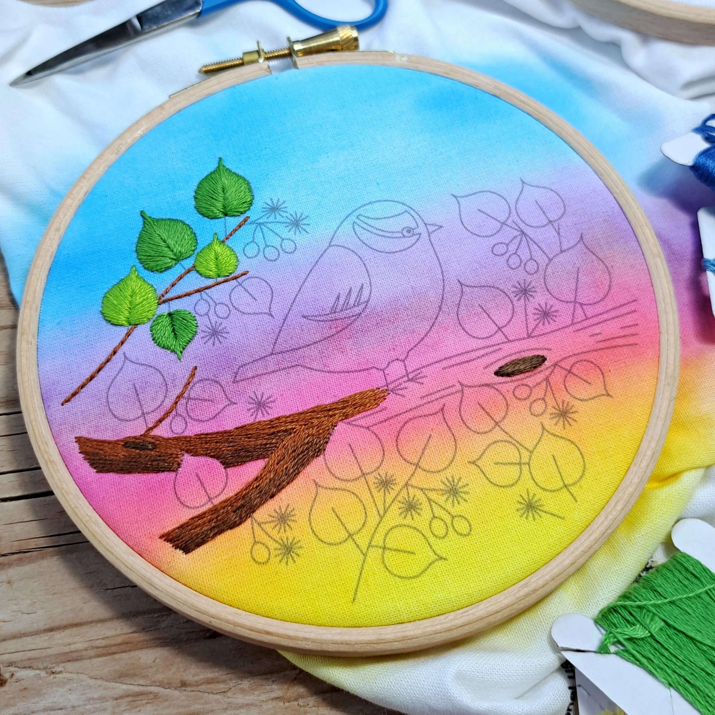 Partly completed embroidery of a tree branch and leaves on a bird embroidery fabric panel.