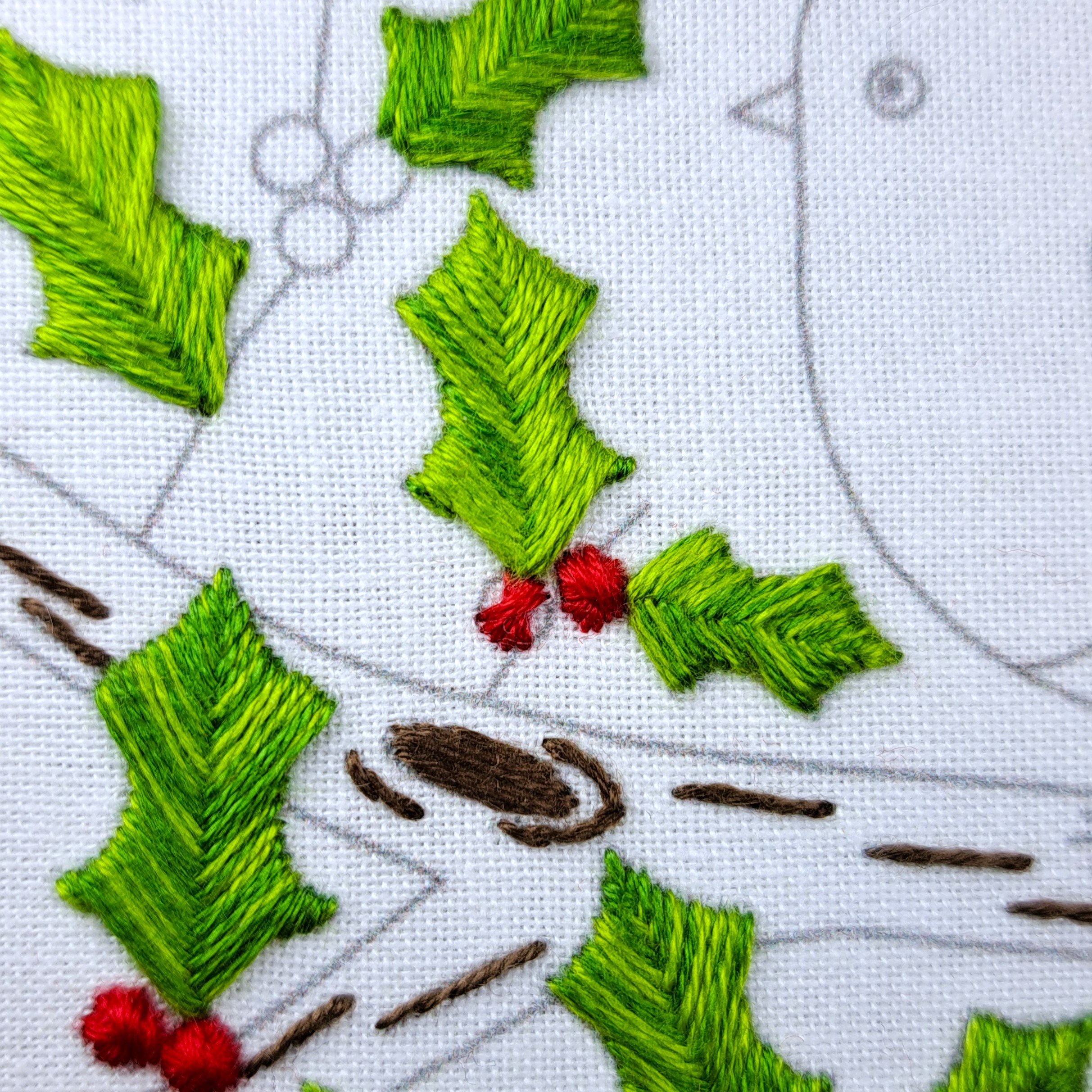 Close-up of a half-stitched red holly berry using Rhodes Circle Stitch.