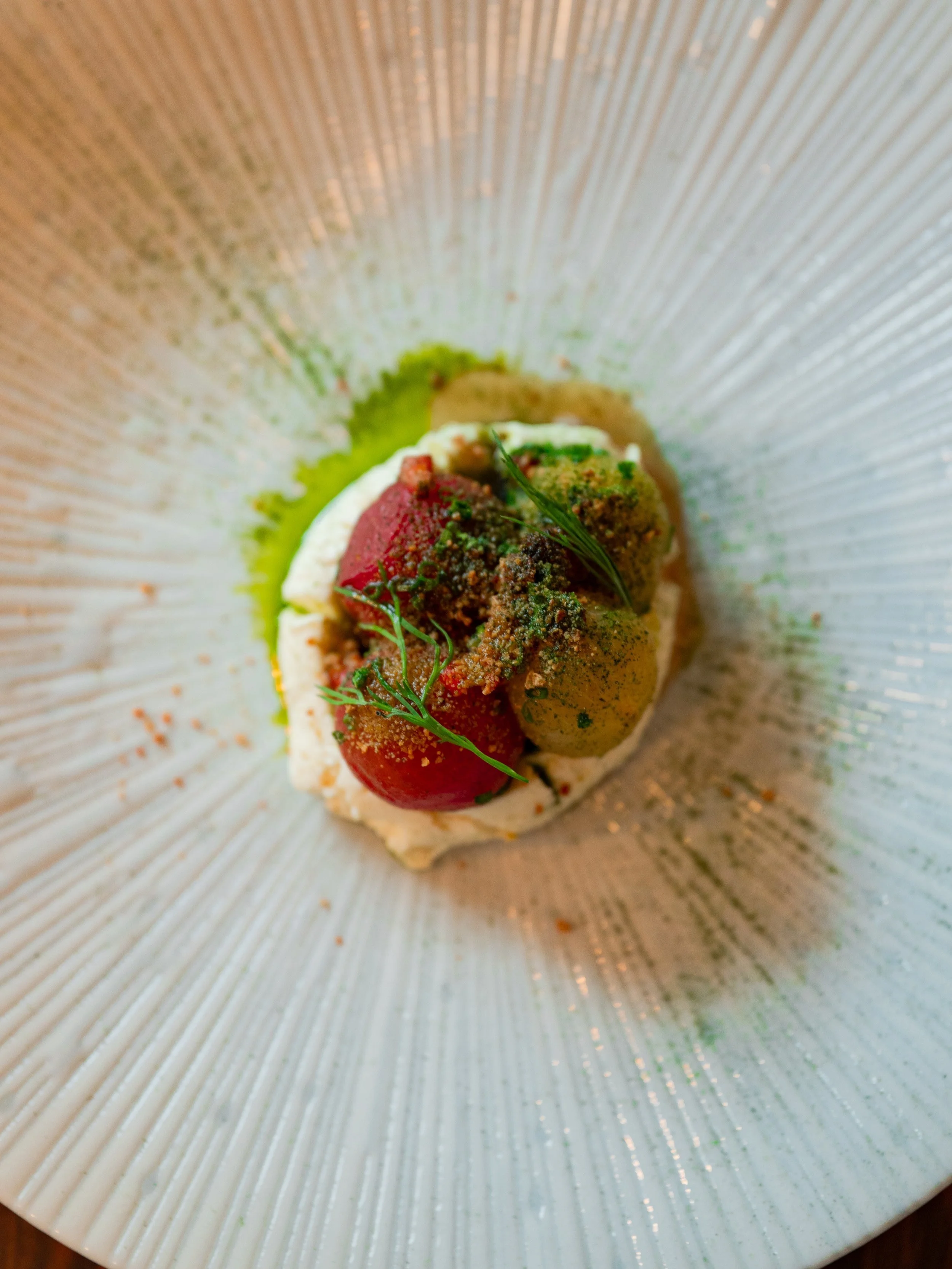 A plated dish with tomatoes, green herbs, and a creamy base, garnished with green oil or sauce and herbs.