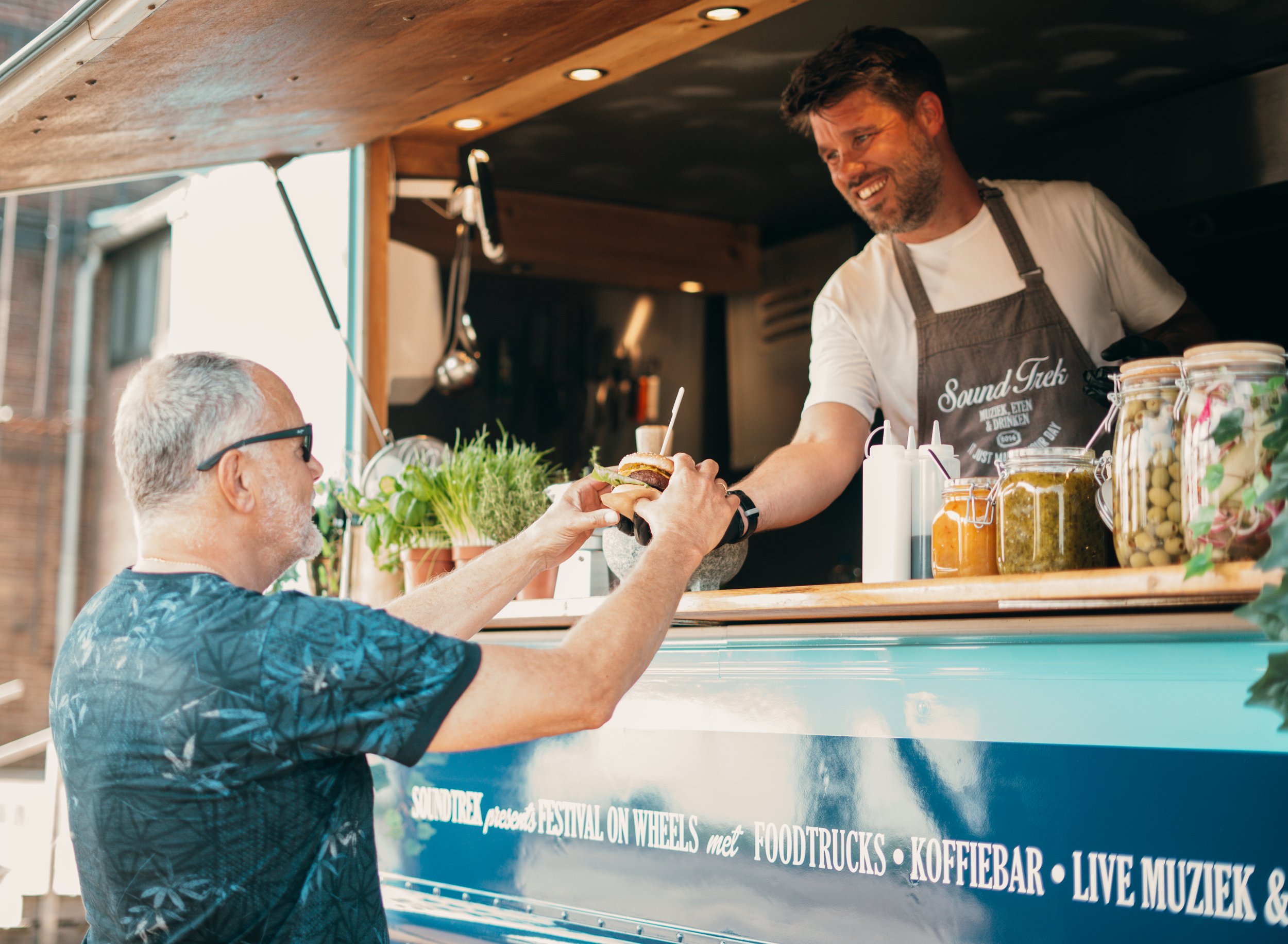 Man ontvangt een burger uit een foodtruck die catering op locatie verzorgd van SoundTrek voor bedrijven