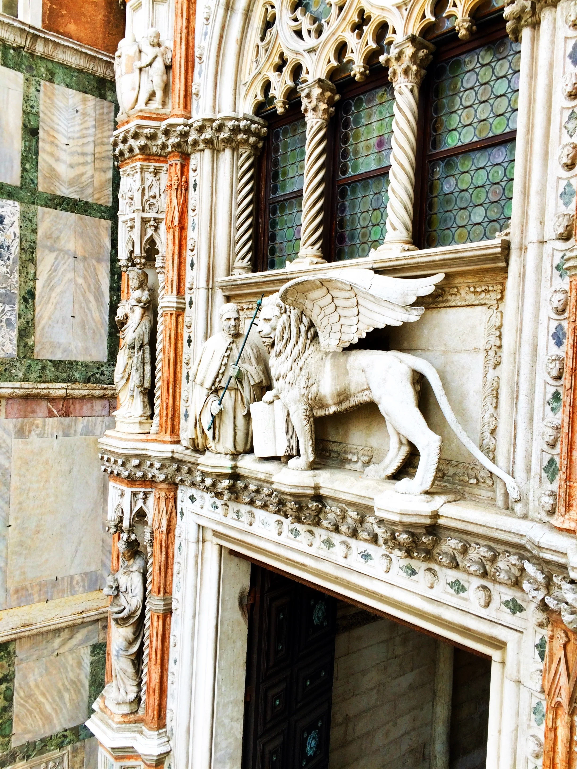  The marble detail of a winged lion (with paw on book) and Doge Francesco Foscari above the Paper Gate of the Doge Palace are in St. Mark’s Square. 