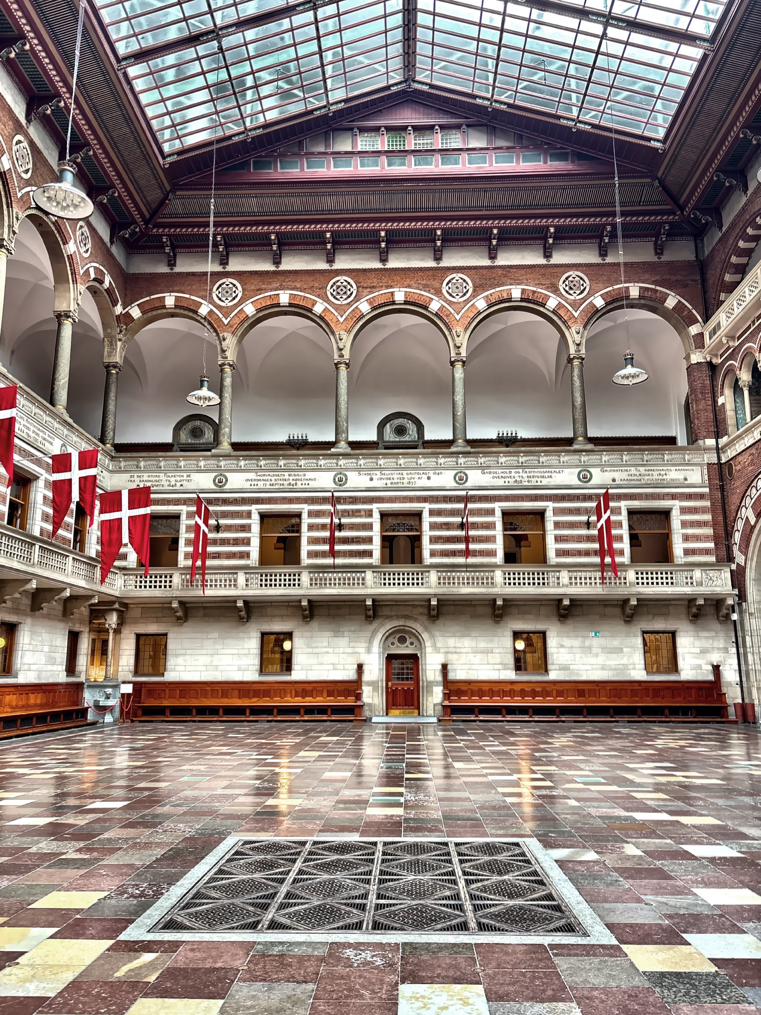  The City Council Hall features tall, ornately decorated walls, a soaring glass ceiling, and vibrant stained-glass windows, reflecting the grandeur of Copenhagen’s civic architecture. 