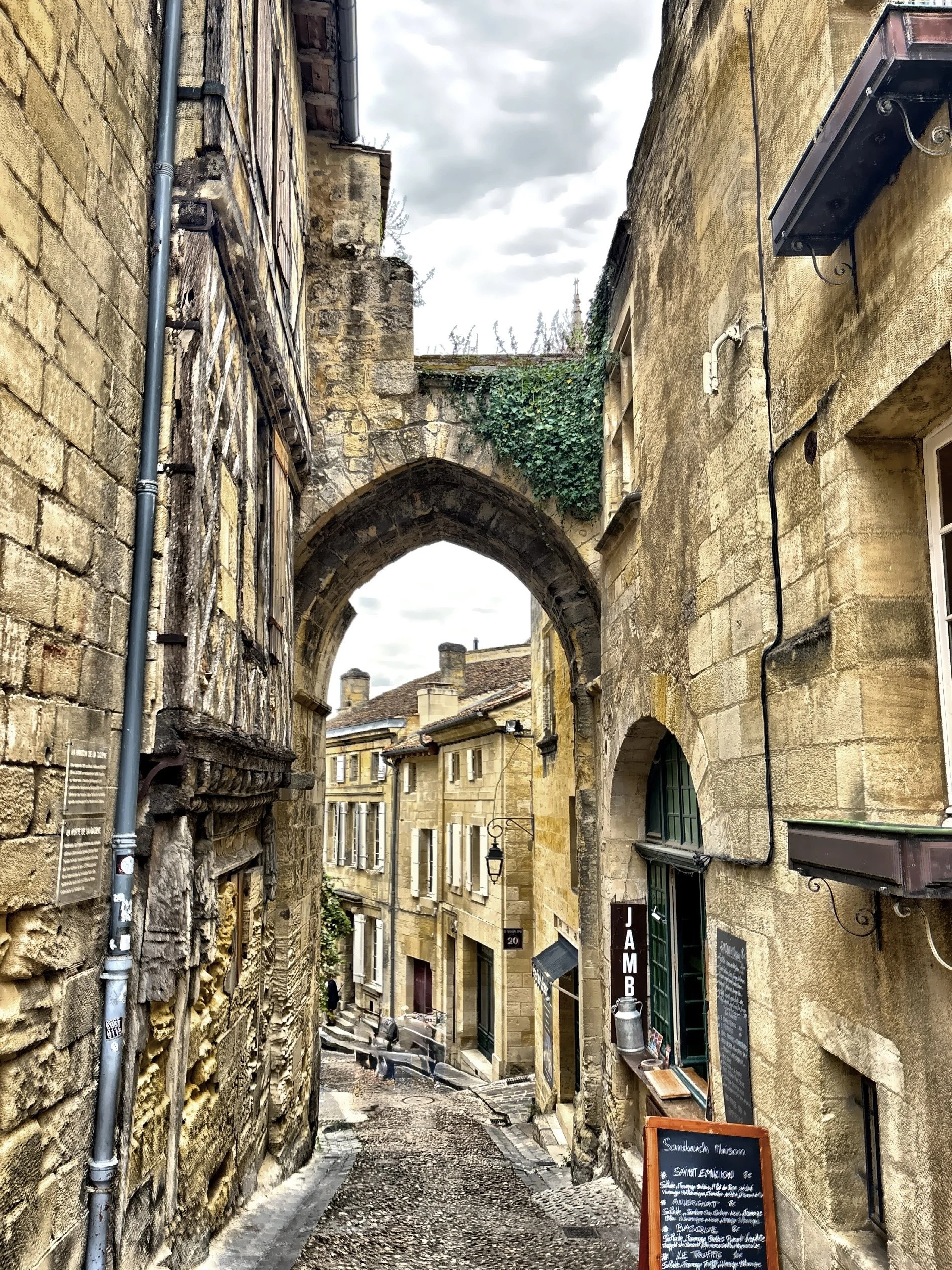  A narrow, sloping cobbled street passing under a stone arch. 