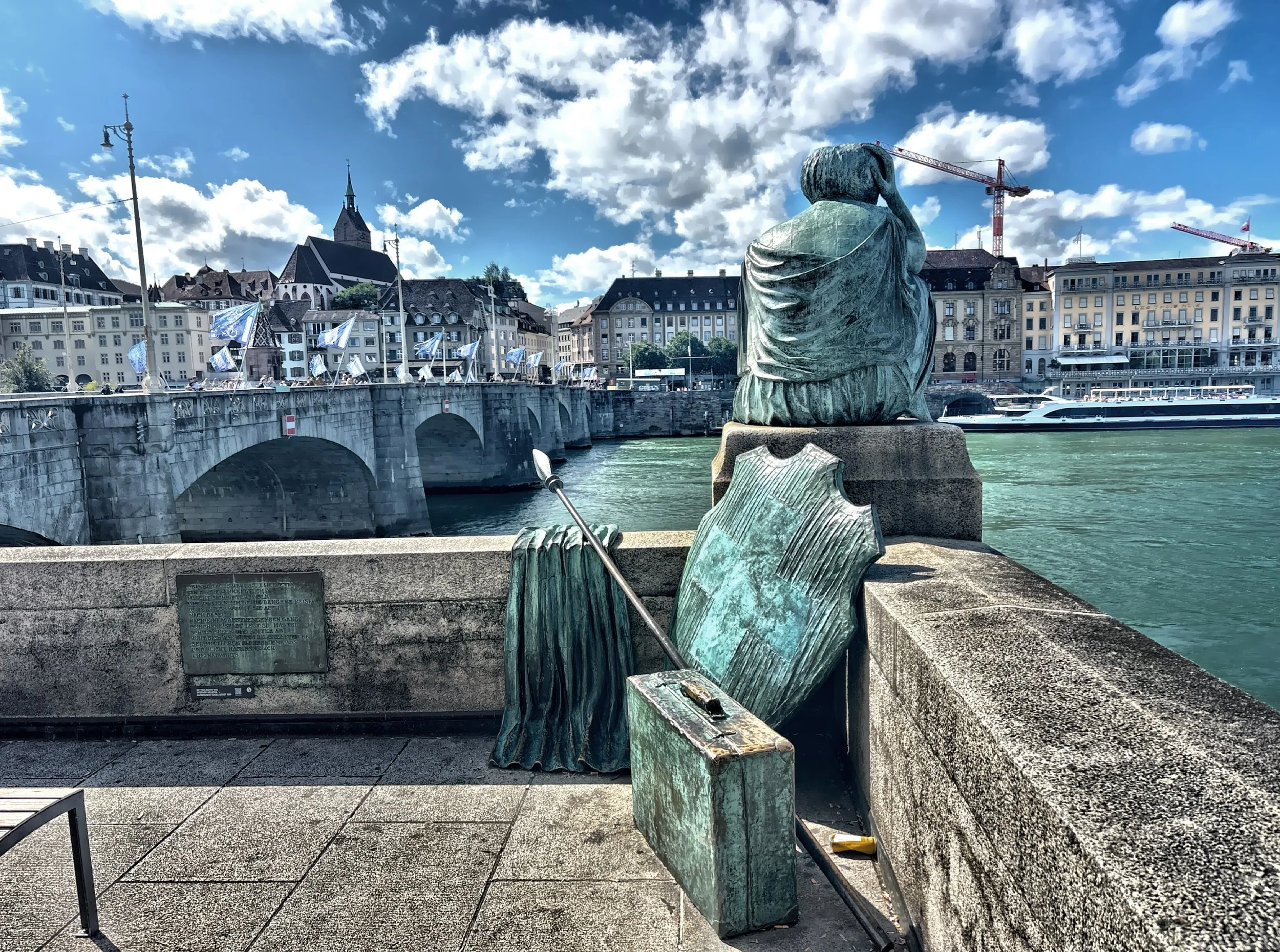  The monument ‘Helvetia Traveling’ depicts Helvetia, the female national personification of Switzerland, seated barefoot with her cape, spear, shield, and a suitcase, gazing across the river toward the Old Town. 