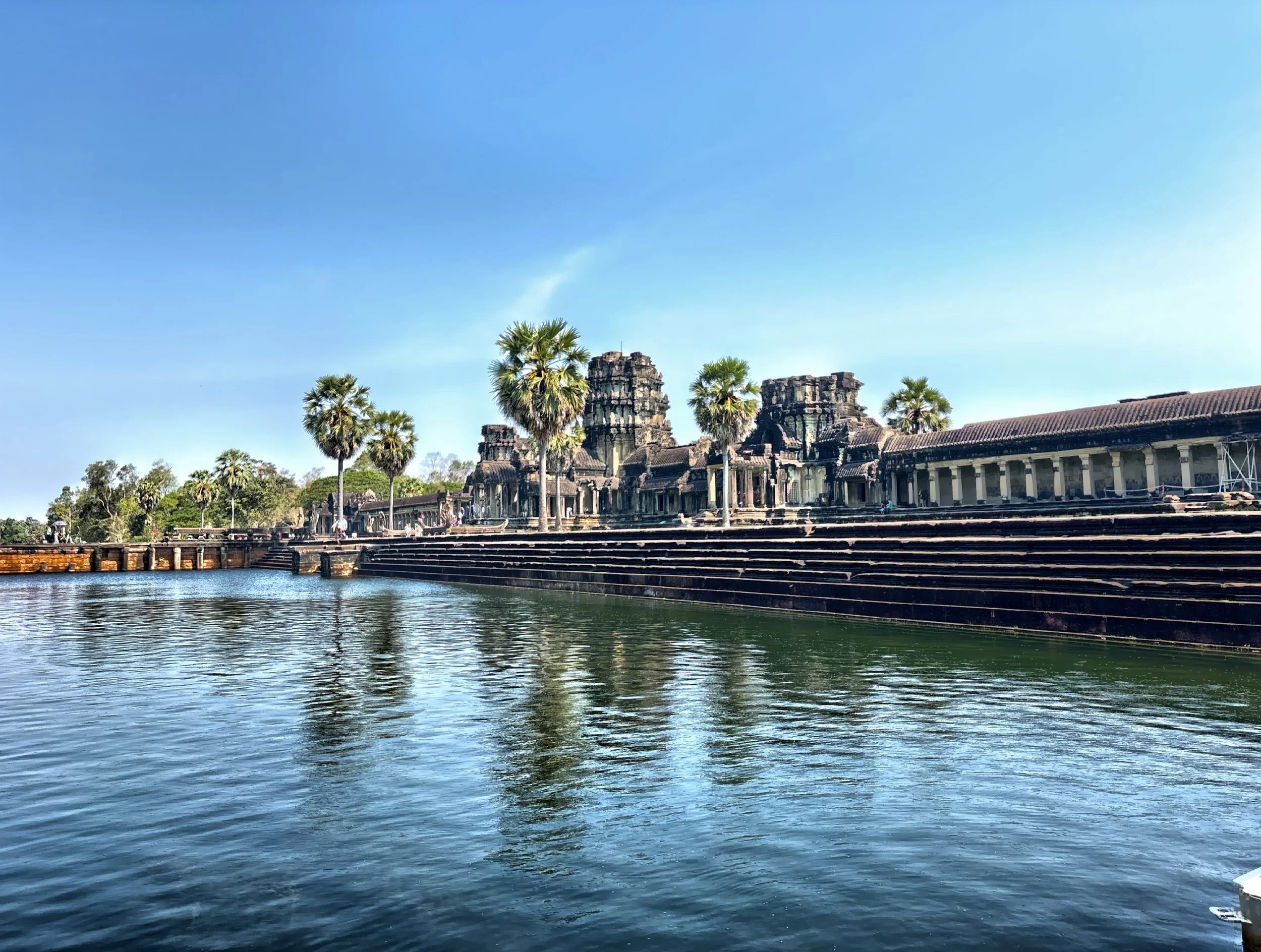  Encircled by a massive moat, the temple rises amid palm trees, the tropical landscape enhancing its timeless grandeur. 