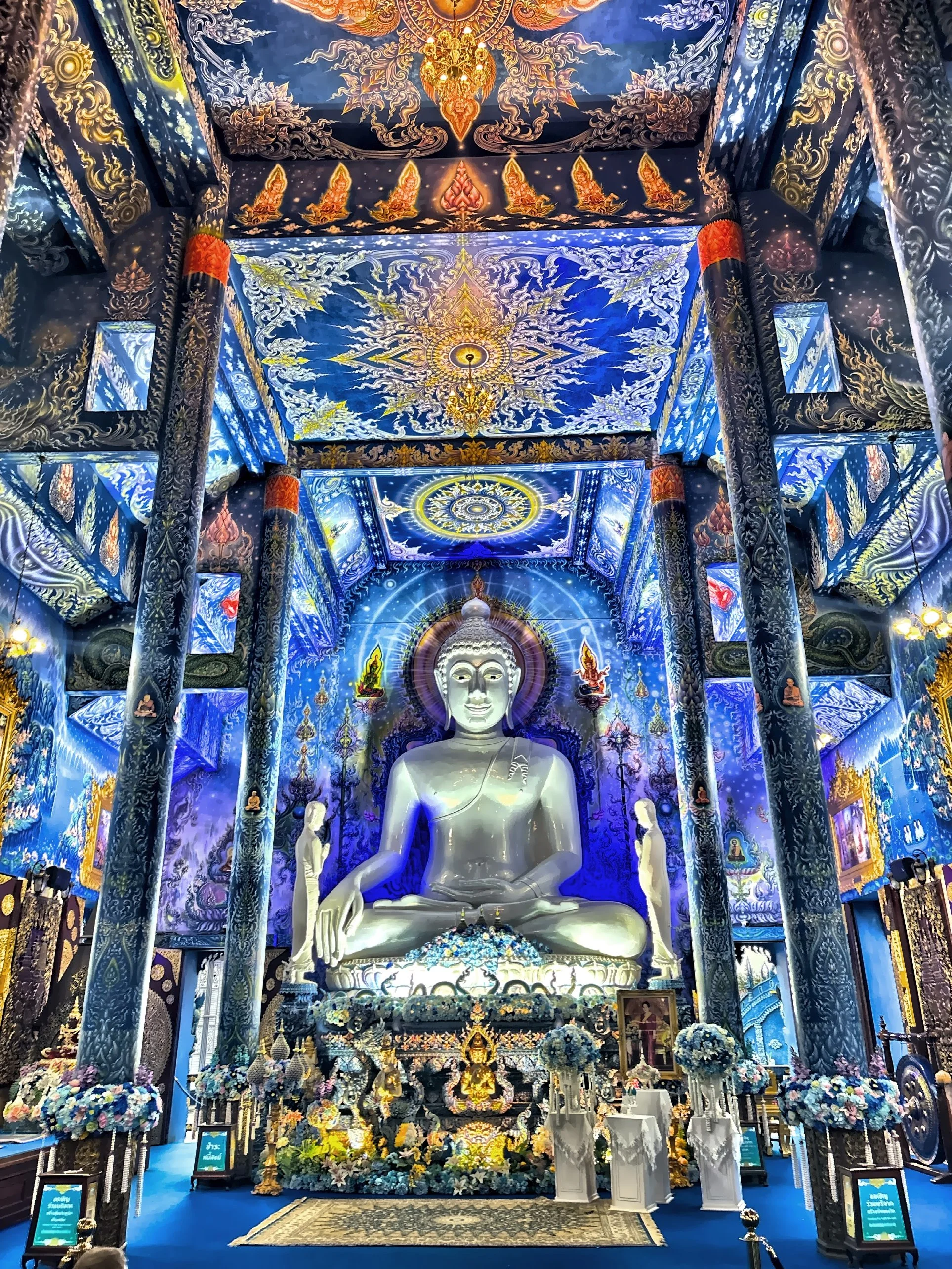  Inside, the atmosphere shifts from dazzling to quietly awe-inspiring. A white Buddha sits serenely at the center, framed by swirling blue murals that stretch across the walls and ceiling. It’s the kind of place where you instinctively lower your voi