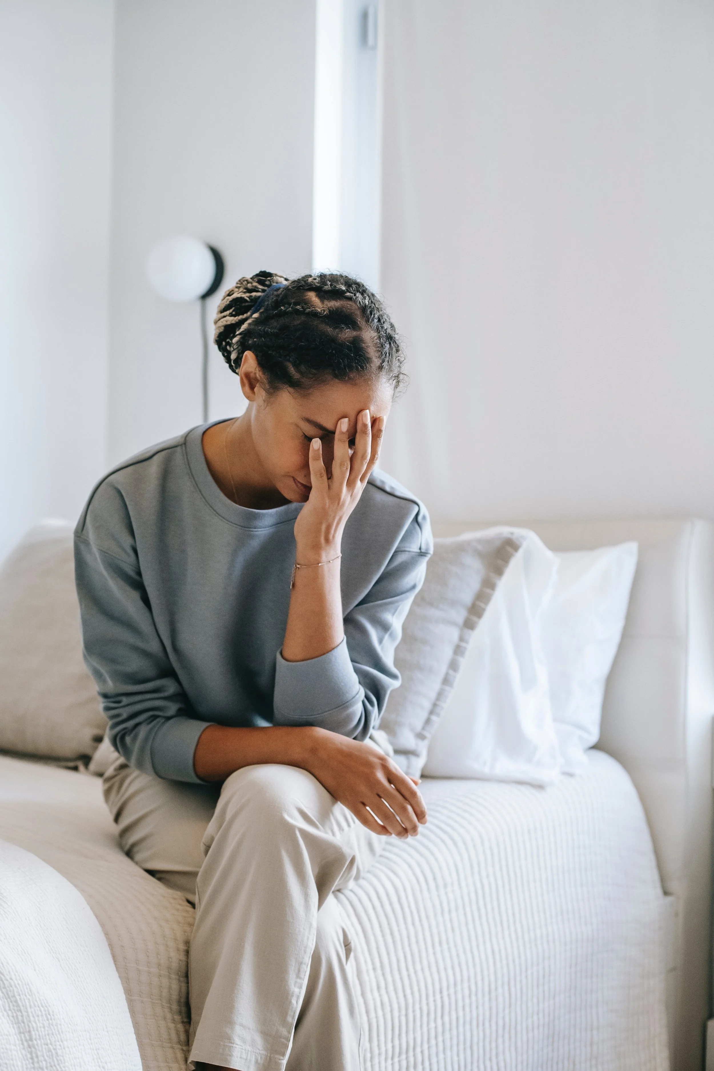 Woman sitting on a bed looking down while holding head in pain