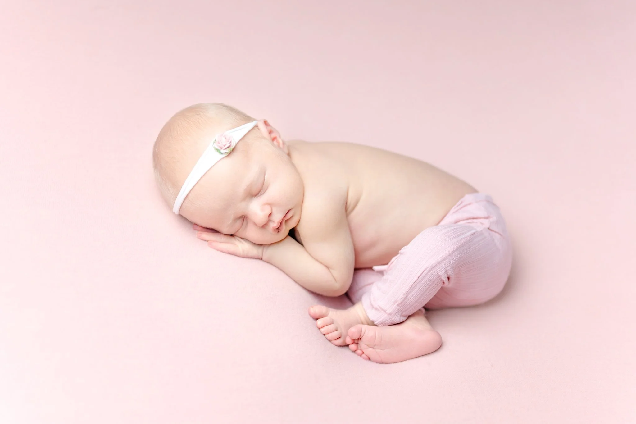 A newborn baby sleeping peacefully on a pink backdrop during her Maryland Newborn Photography Session