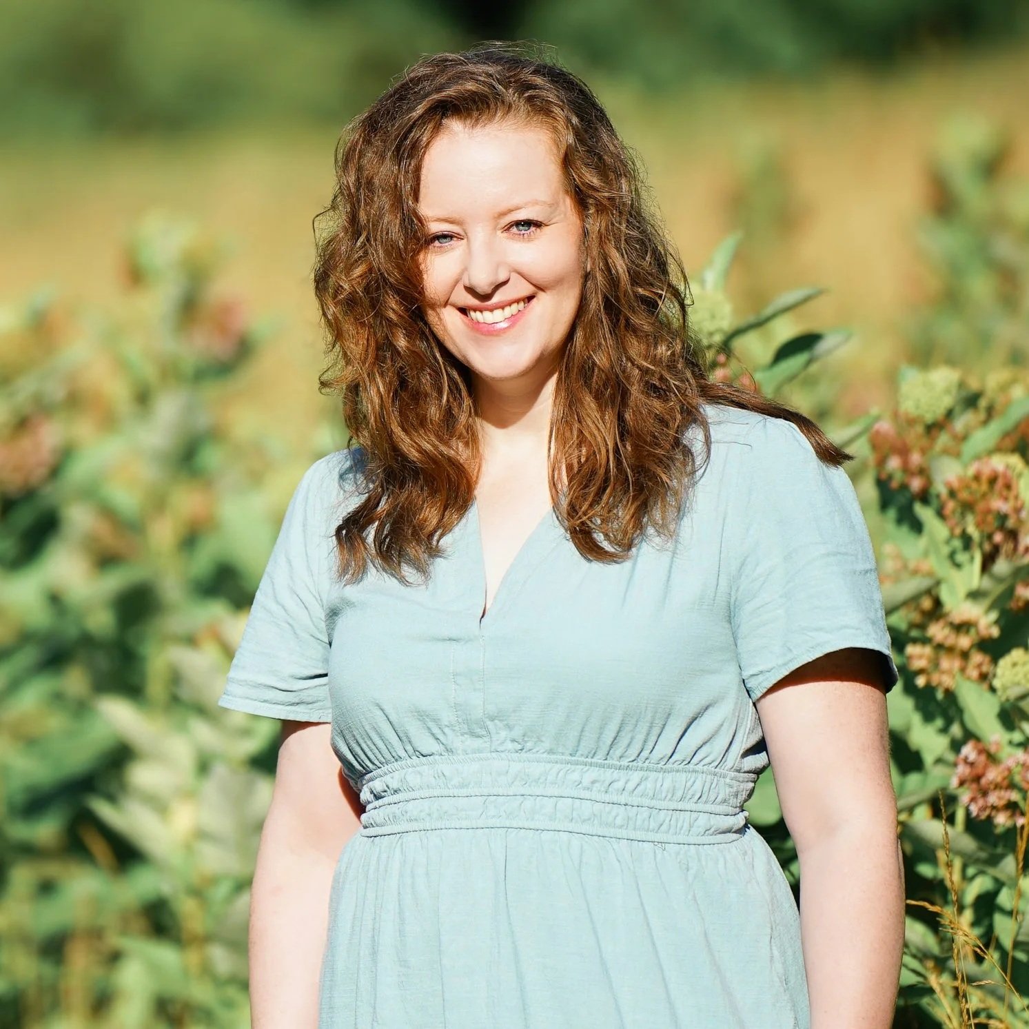 Casey Elaine, an APNPI safety-certified newborn and maternity photographer based in Anne Arundel County, Maryland, smiling in a sunny field..