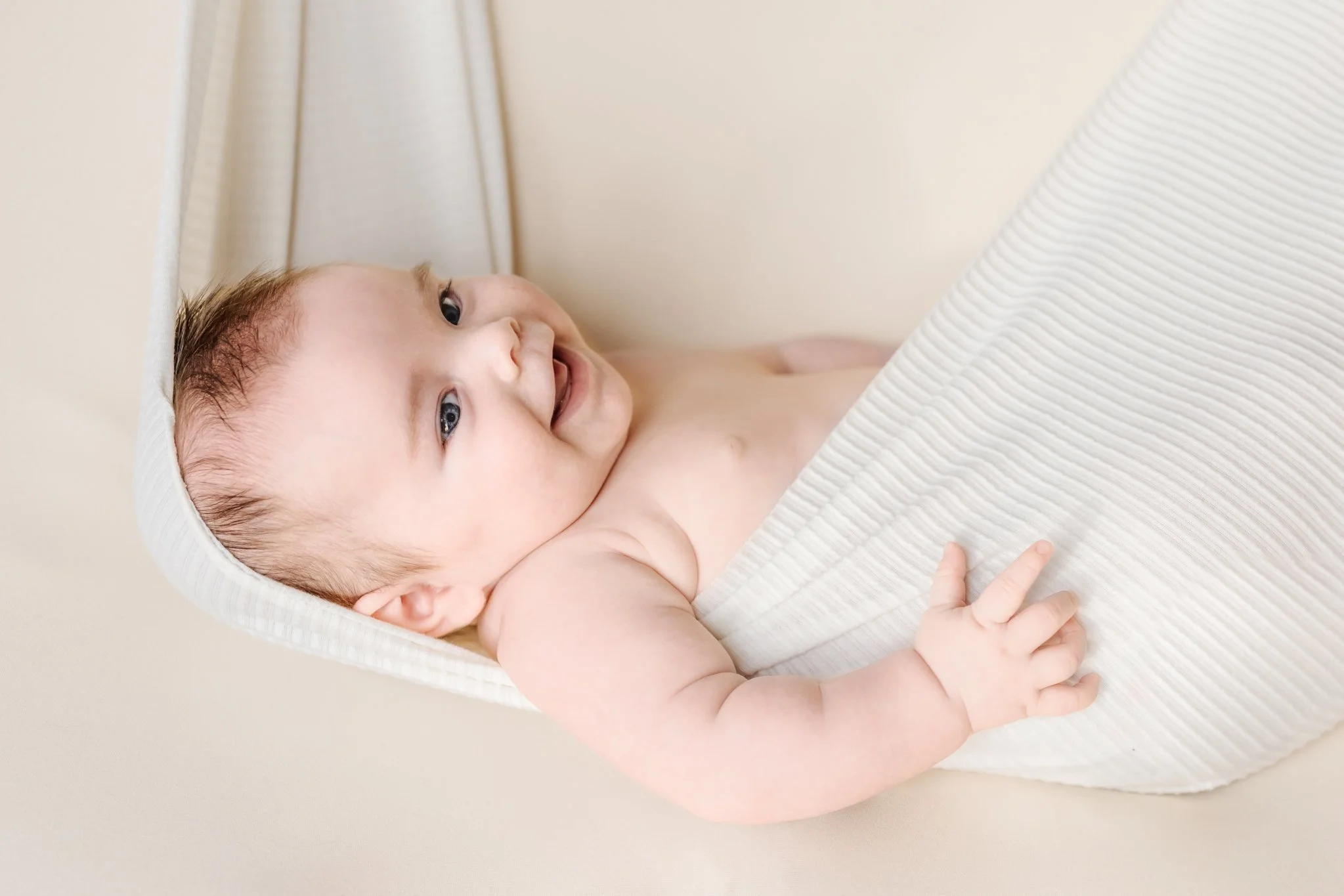 A Newborn baby is posed in a prop hammock on a cream backdrop during his Maryland newborn photography session