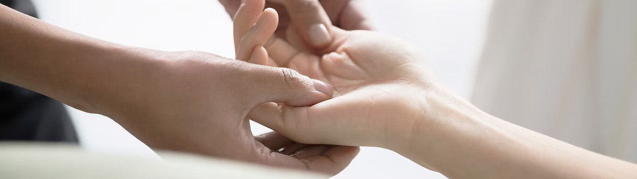 Two people holding hands, with one person gently clasping the other's hand.