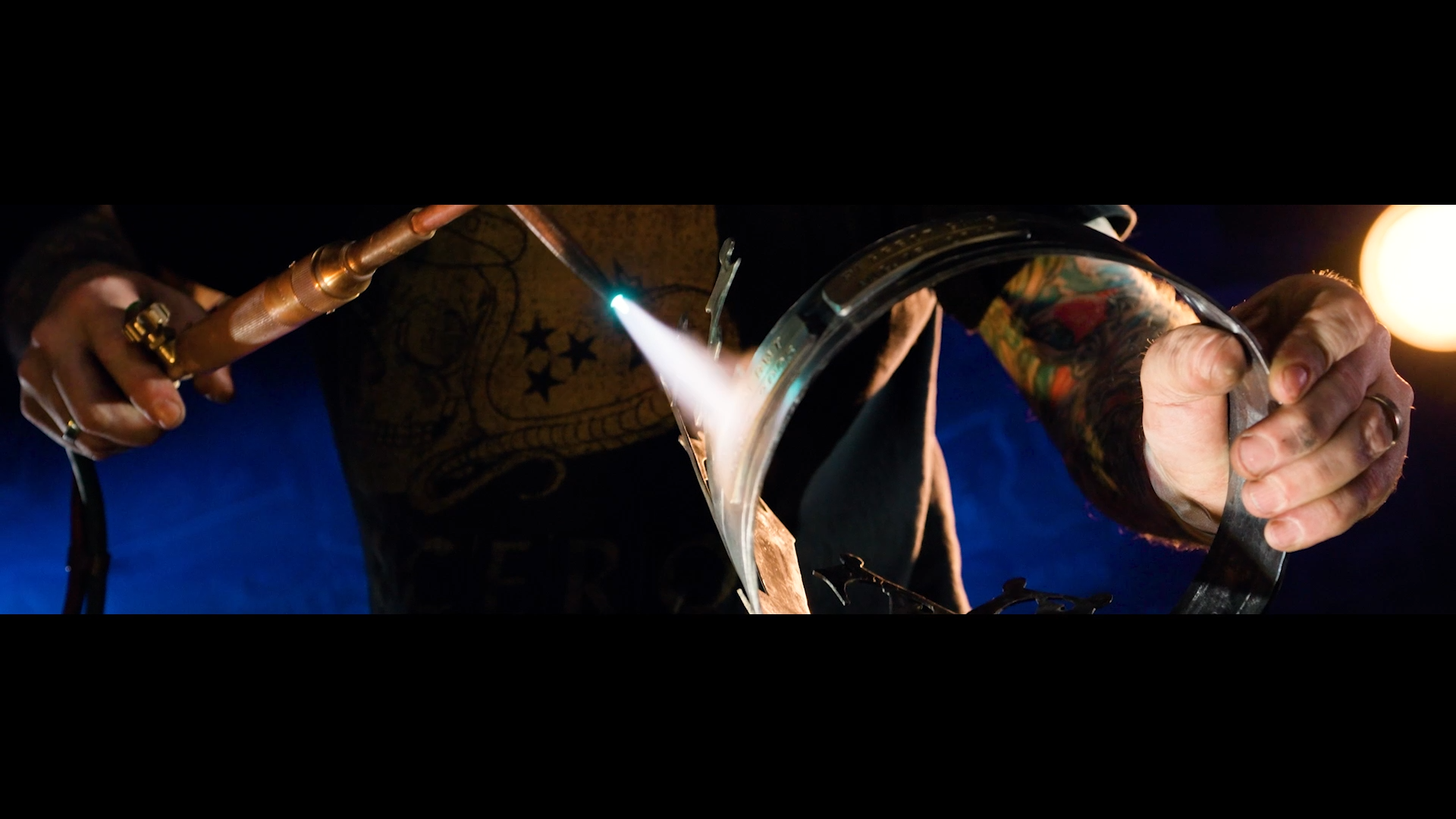 Toward the end of the crown process, we're back to blue in the background, but the flame of the blowtorch and the crown are featured prominently in front. I shot this wide enough to also capture the texture of the torch, and the blacksmith's hands an