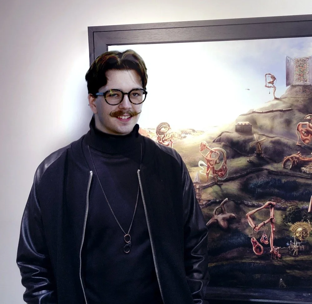 Person wearing glasses and a dark jacket stands beside a surreal painting with abstract shapes and landscapes in an art gallery setting.