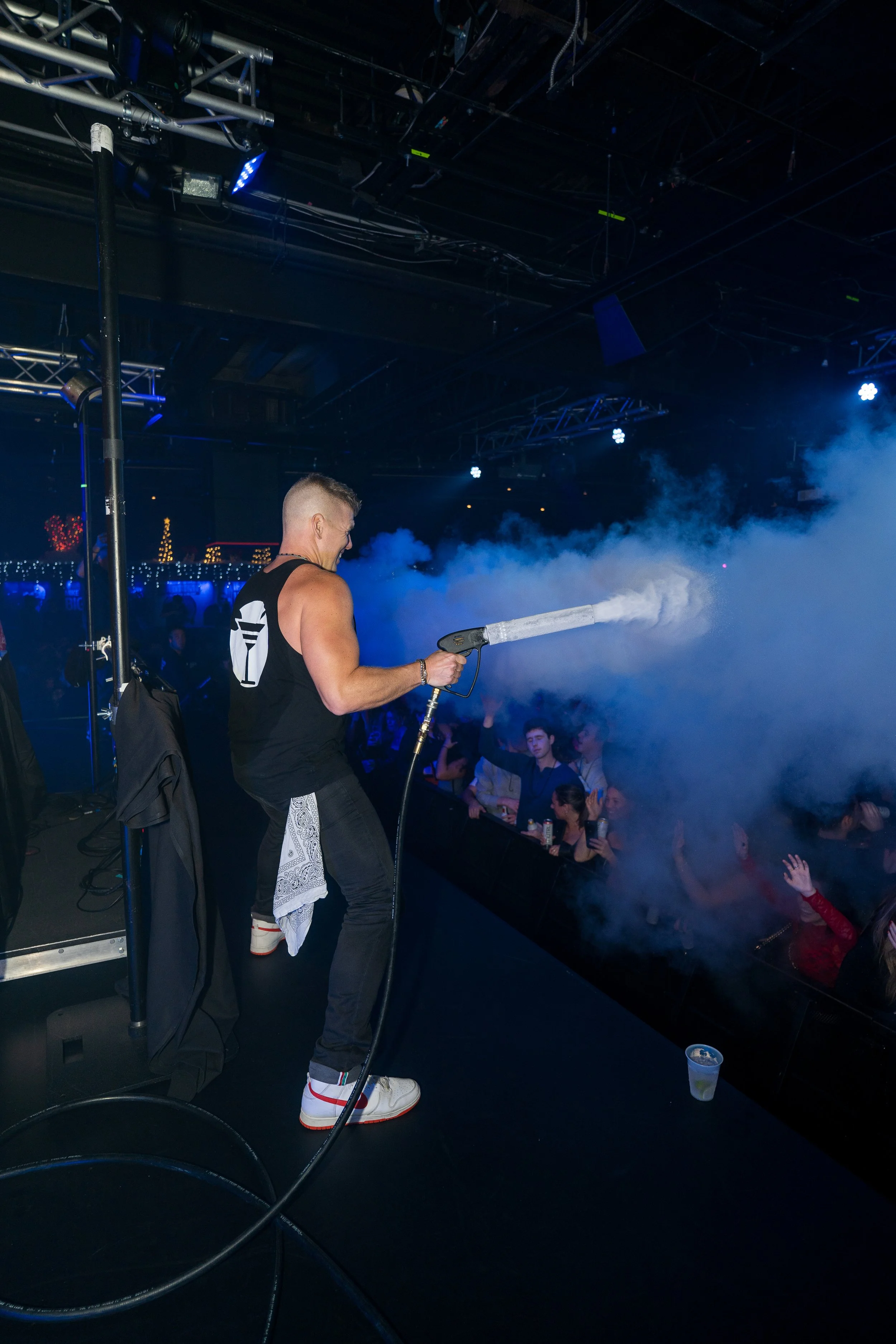 DJ spraying fog or smoke at a nightclub or concert while audience watches.
